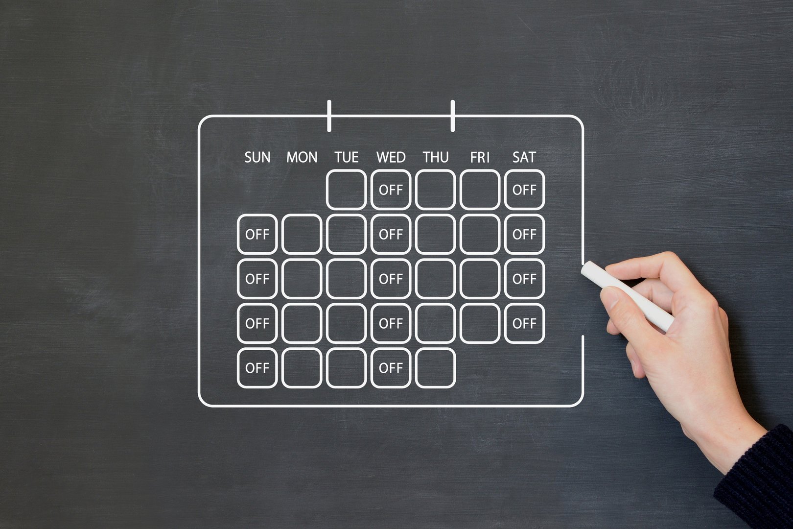 A person drawing a calendar on a blackboard that reflects a three-day work week