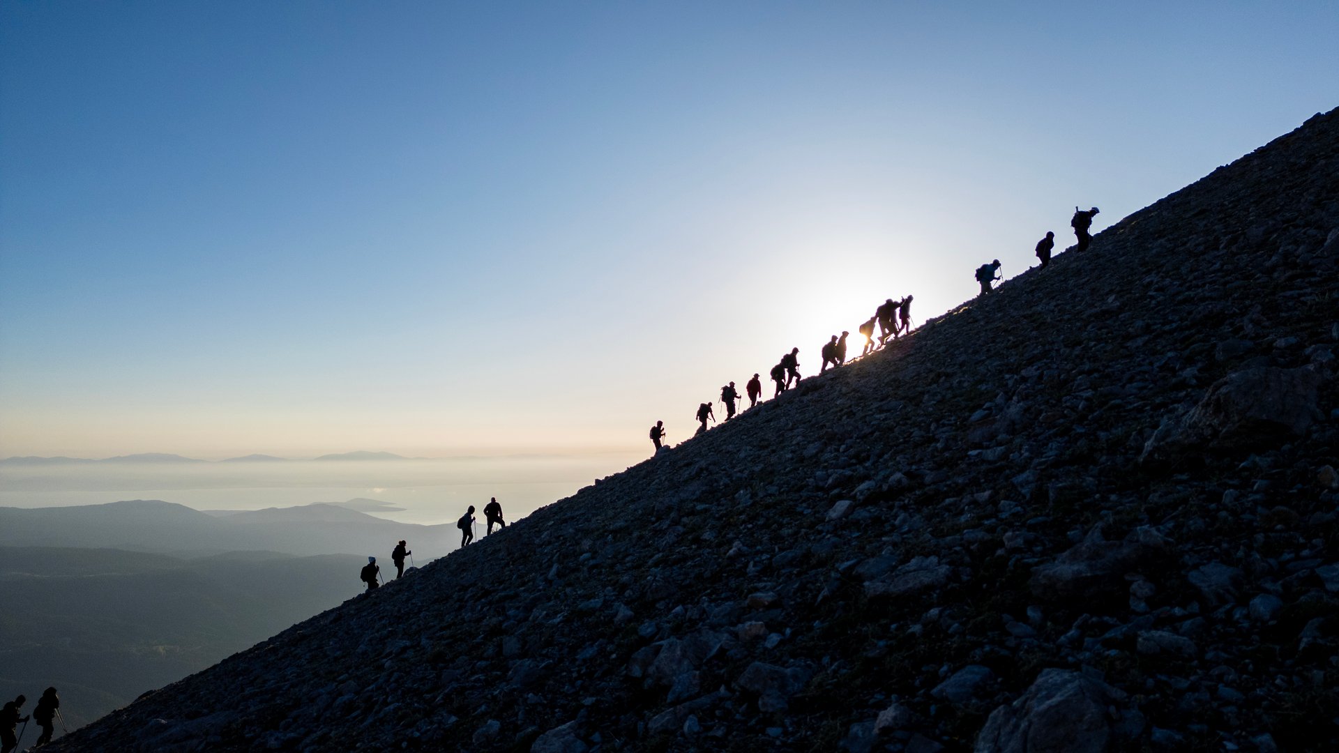Professional crowded team of mountaineers are walking on sloping mountains and enjoying wonderful views