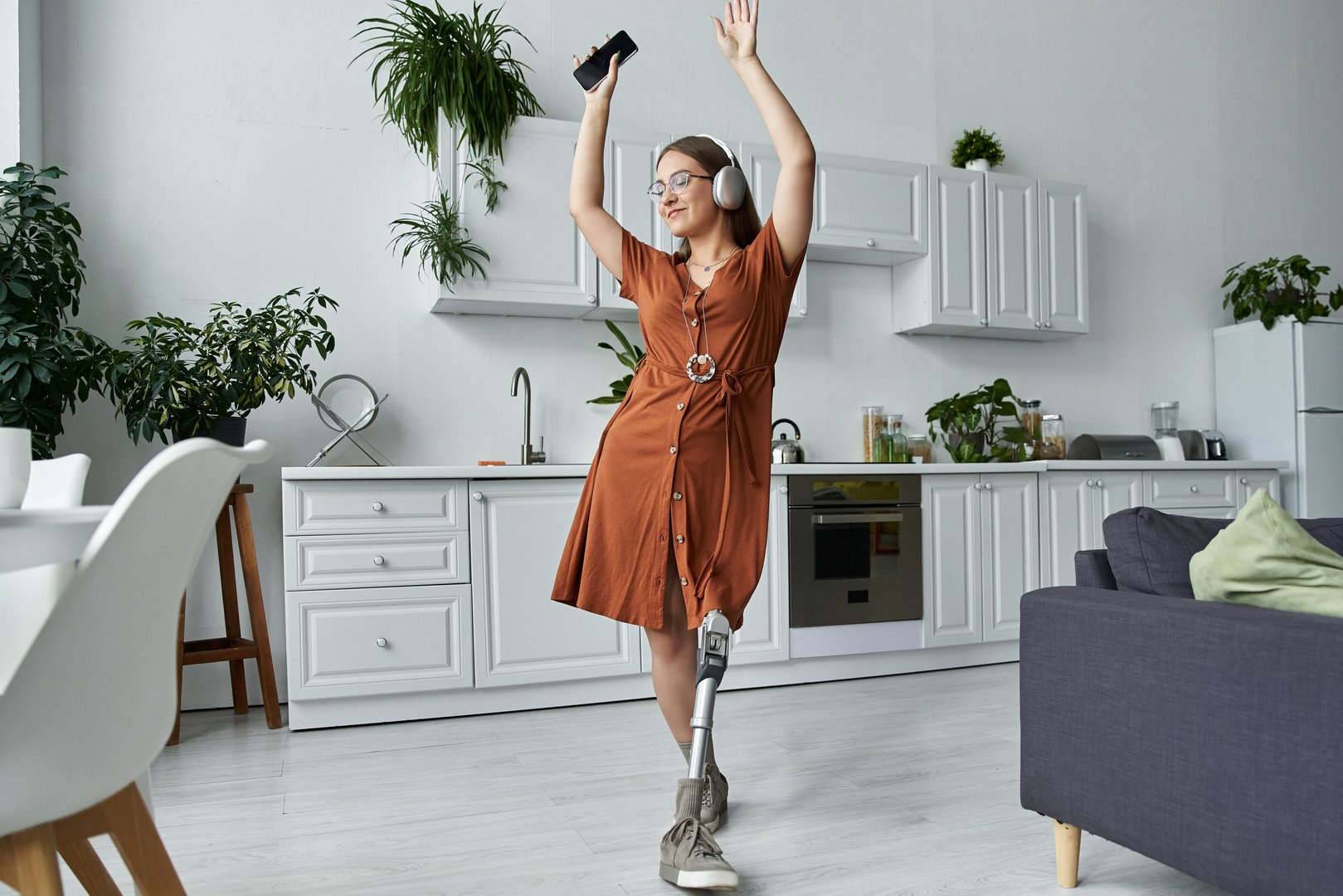 Young woman enjoys music and dances joyfully in her stylish kitchen while wearing headphones.