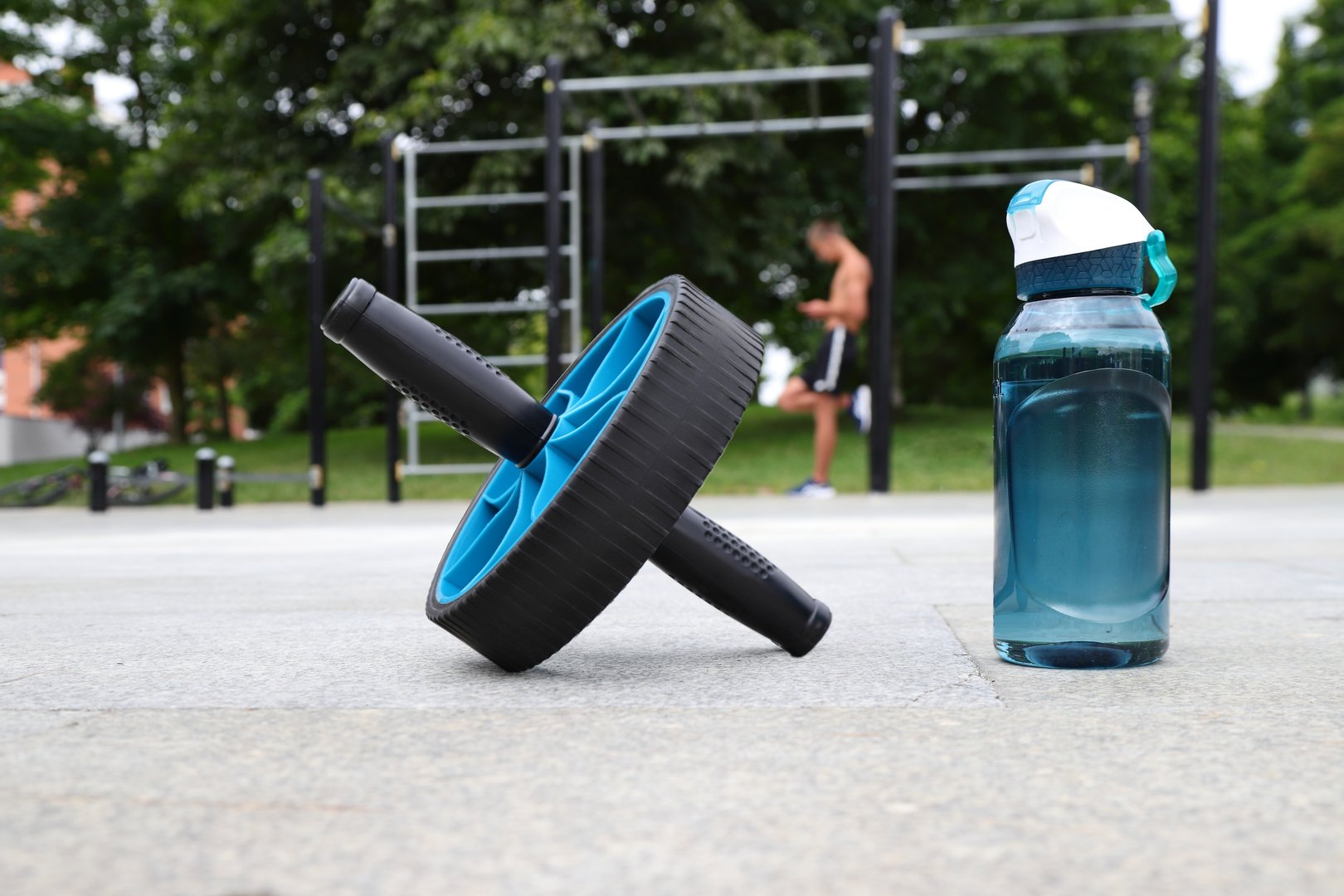 Abdomen wheel and sport water bottle on horizontal bar background, workout outside concept