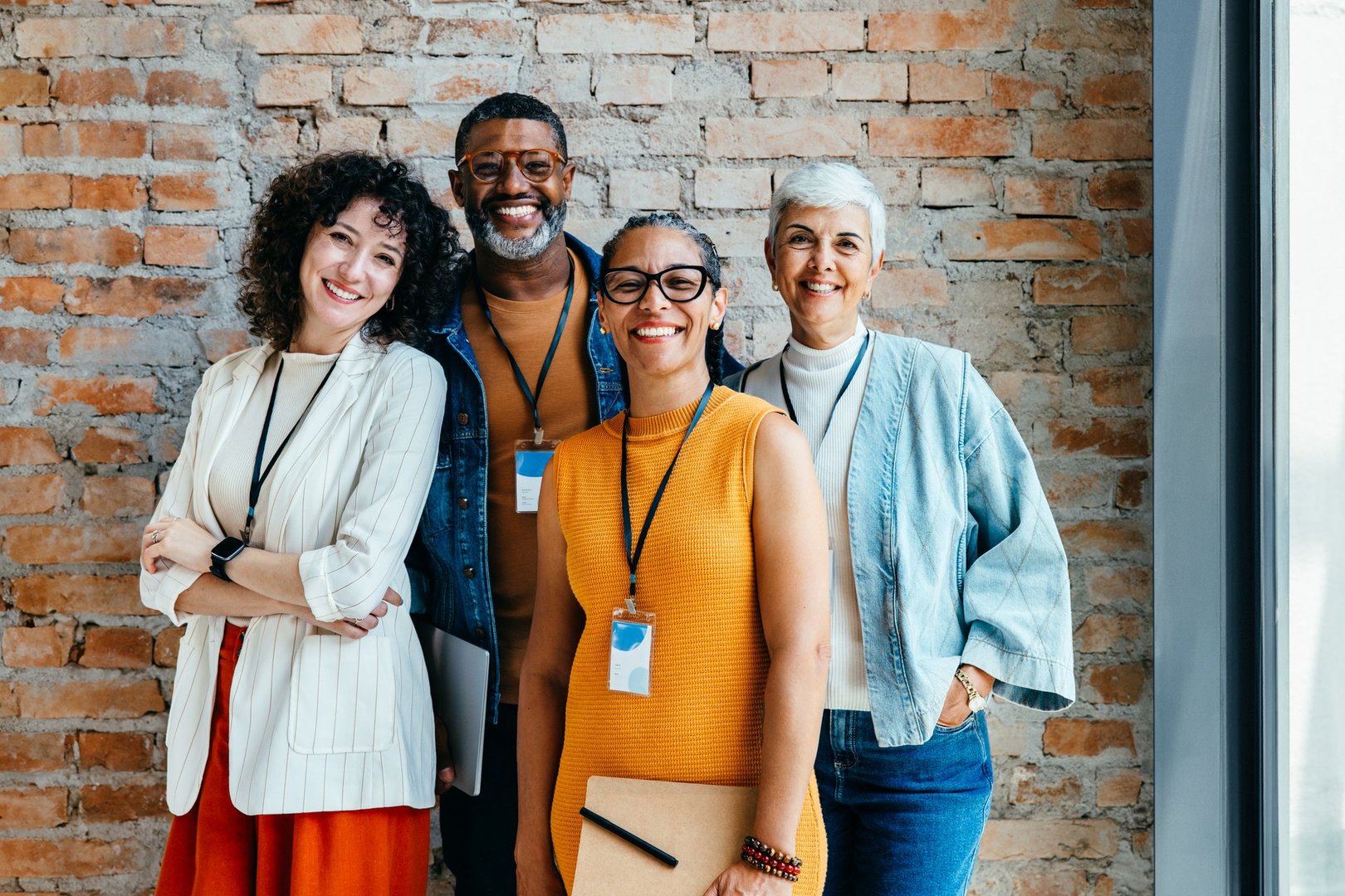 A cheerful and confident group of diverse individuals stand together in an office setting, exemplifying teamwork and a collaborative work environment.