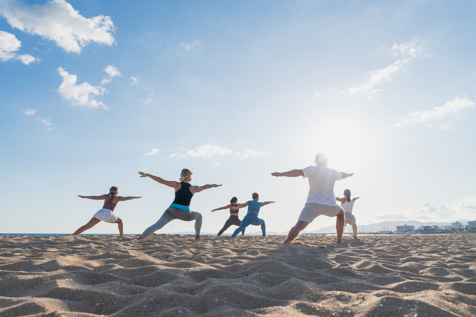 Diverse group holding warrior pose on sandy beach. Concept of yoga, strength, active lifestyle.