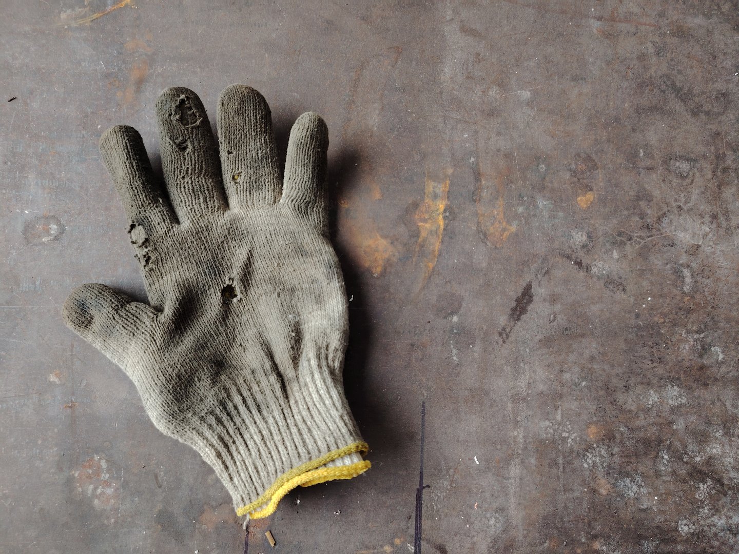 Worn and dirty cotton work glove on a grungy, dark metal surface.