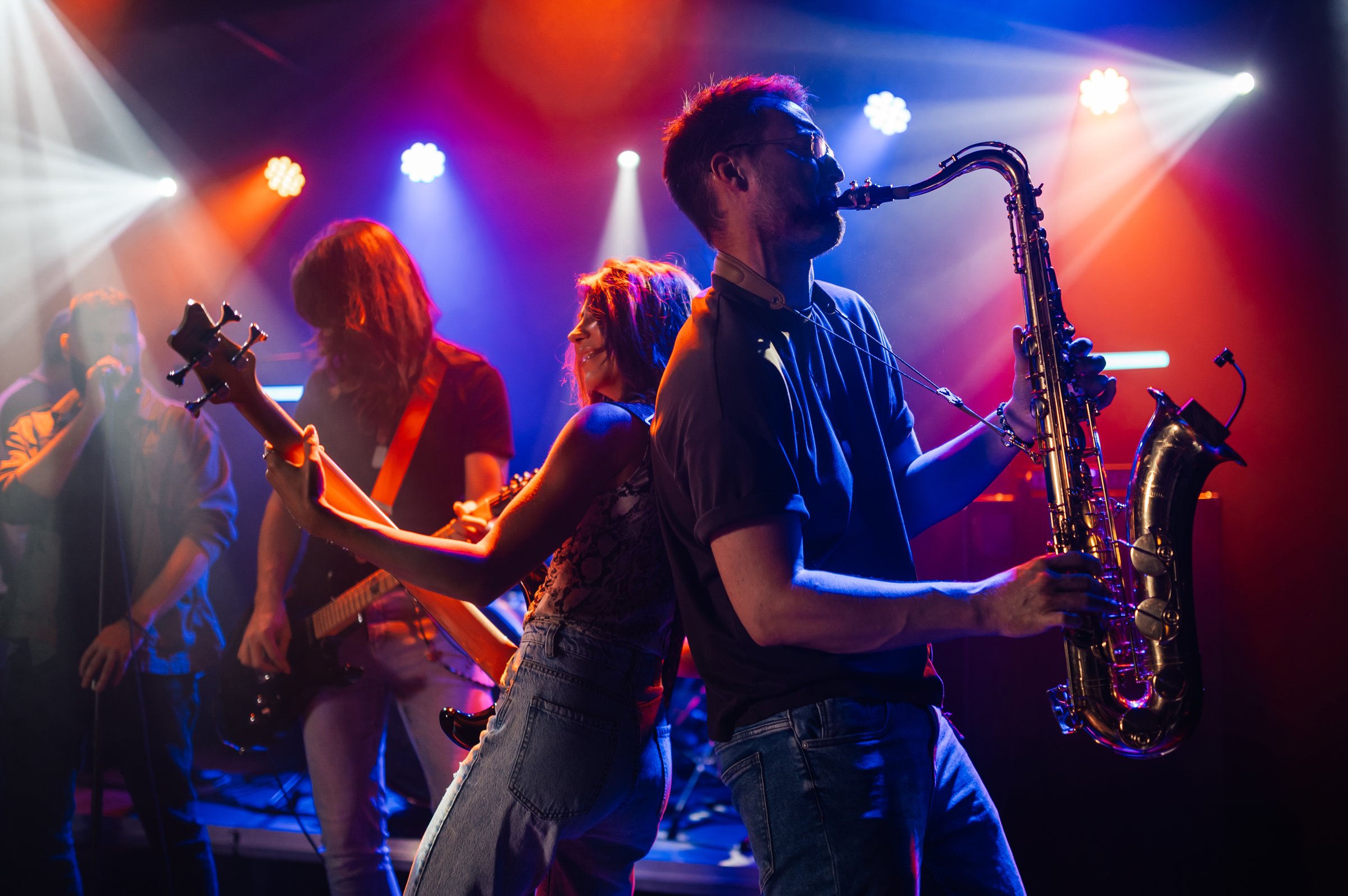 Musicians playing instruments on stage at live concert, saxophonist and bassist back to back, colorful lights creating vibrant atmosphere