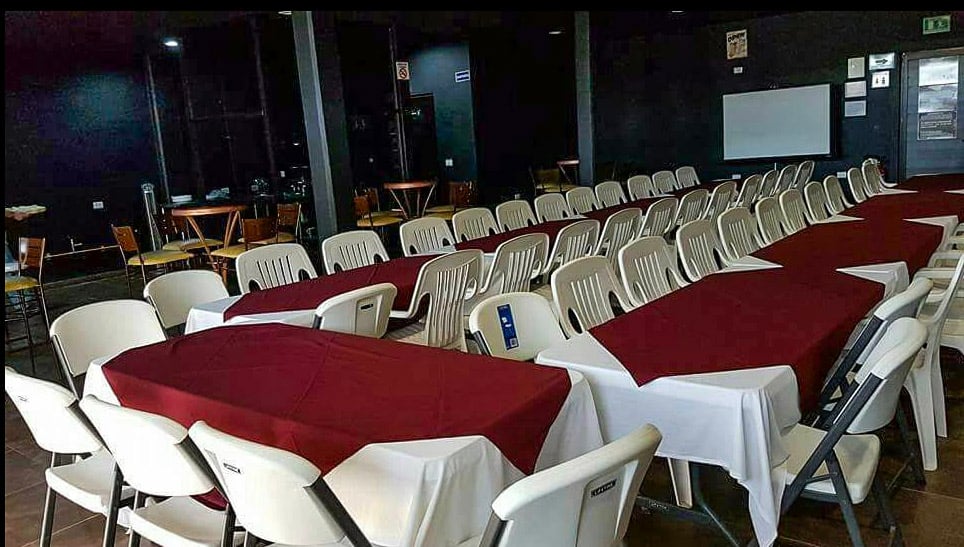 Empty event hall with long tables covered in burgundy and white tablecloths, surrounded by white plastic chairs.