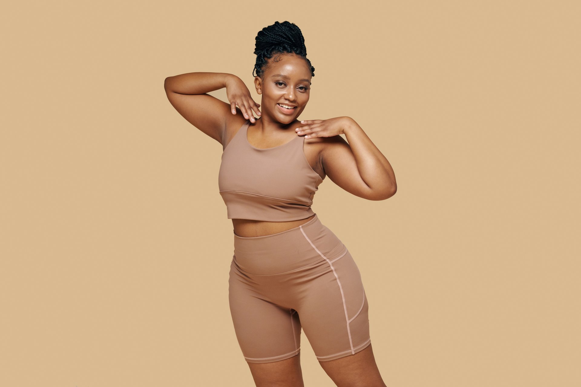 Portrait of smiling fit curvy woman dancing against beige background