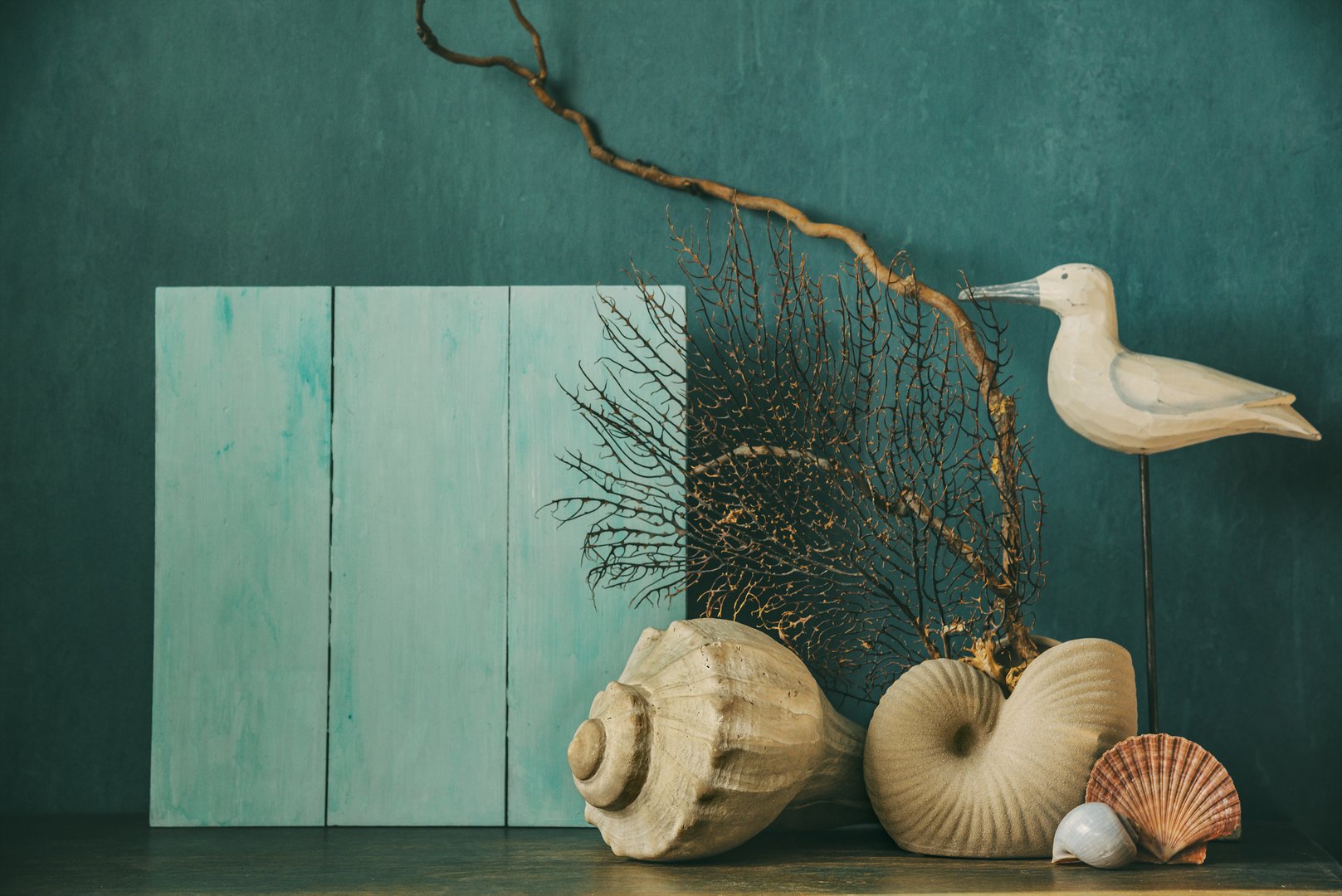 Nautical themed mockup, home decor concept. Composition of seashells and dry natural coral with decorative figurine of seagull on table against blue wall