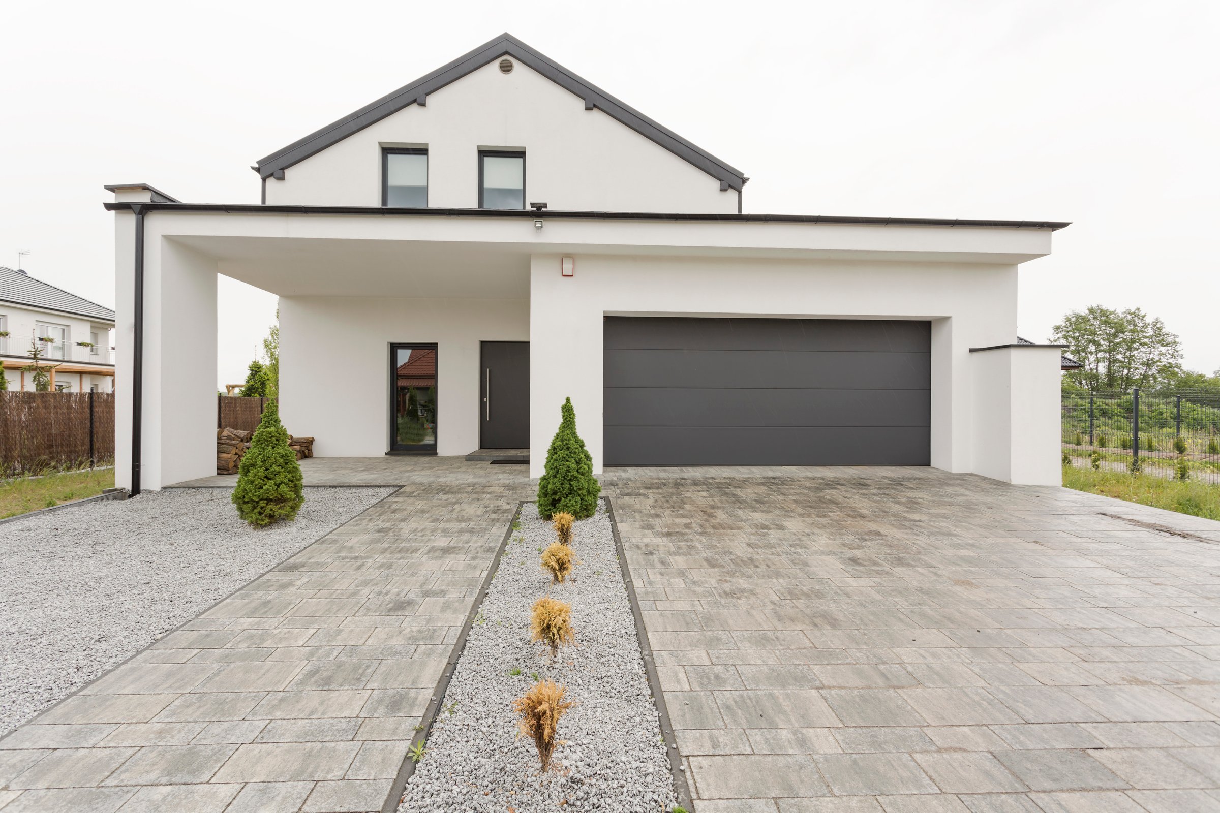 Exterior view of a modern white mansion with a garage and stone driveway