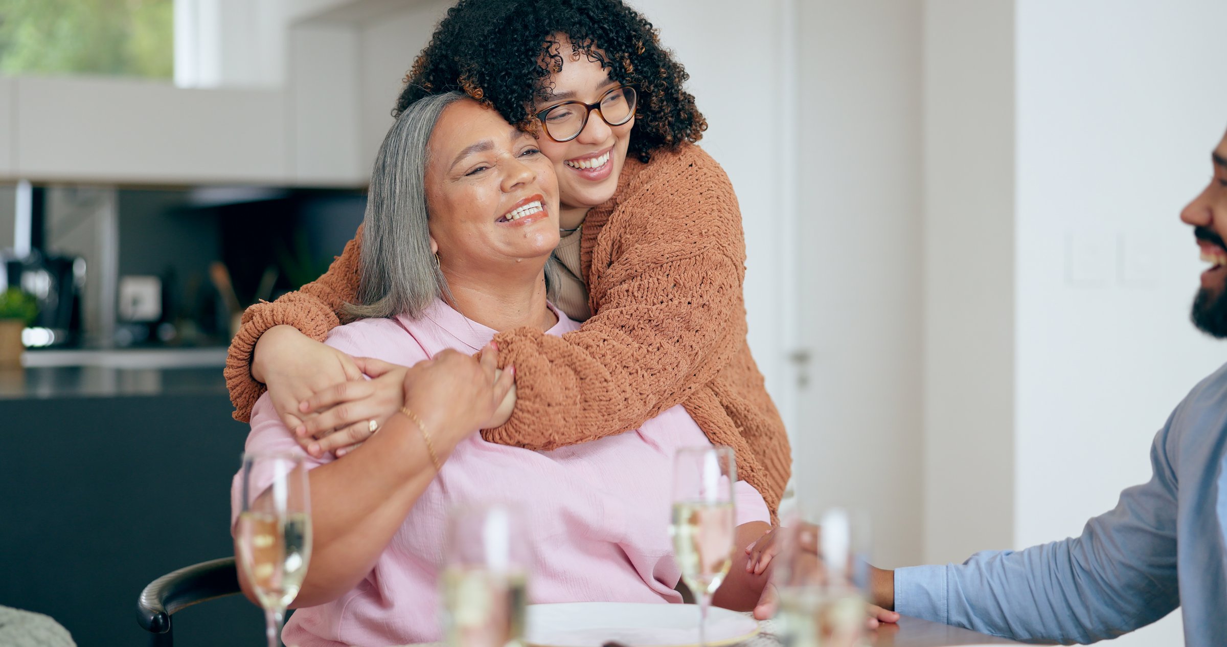 Senior, woman or daughter with hug for love, laugh or joke in dining room of home with happiness. Family, mother and woman with embrace, smile and care for relaxing, peace and comic in lounge of home