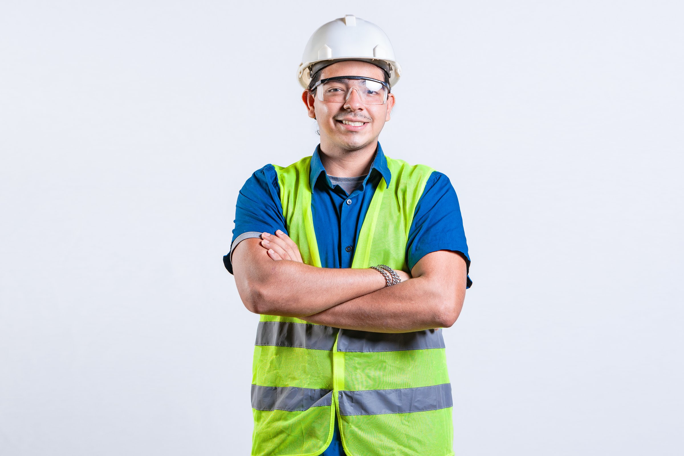 Portrait of smiling latin engineer with arms crossed isolated. Young latin engineer with helmet and vest isolated
