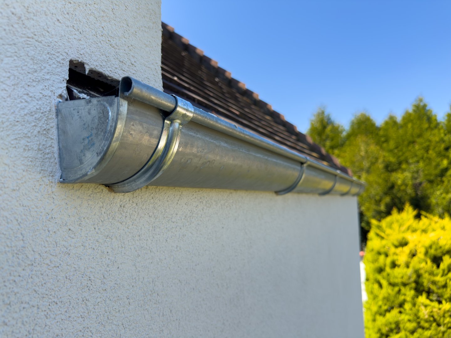 A new metal gutter is fixed along the edge of a home, reflecting sunlight.