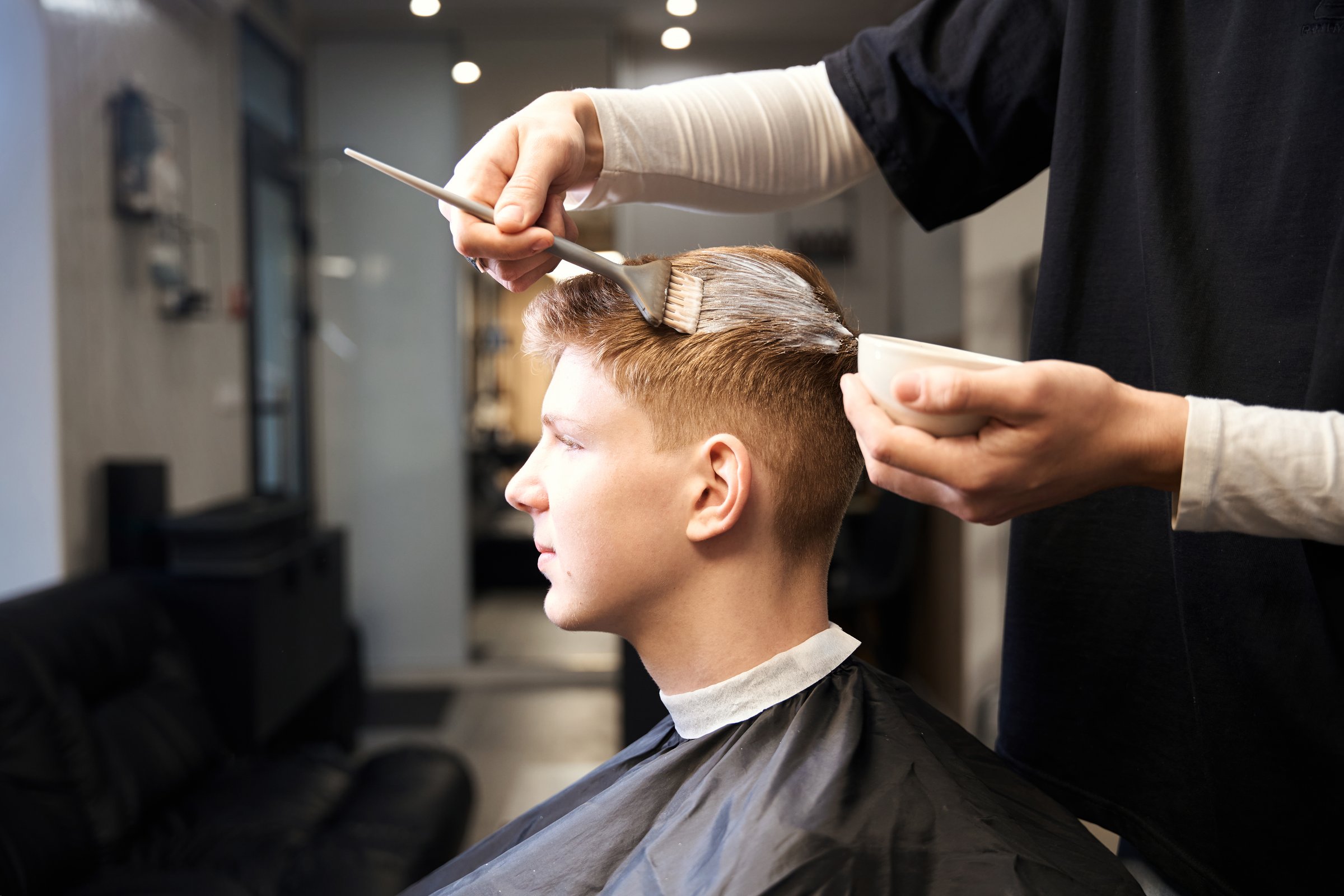 Side view of skilled barber working with hair of young male client in modern barbershop