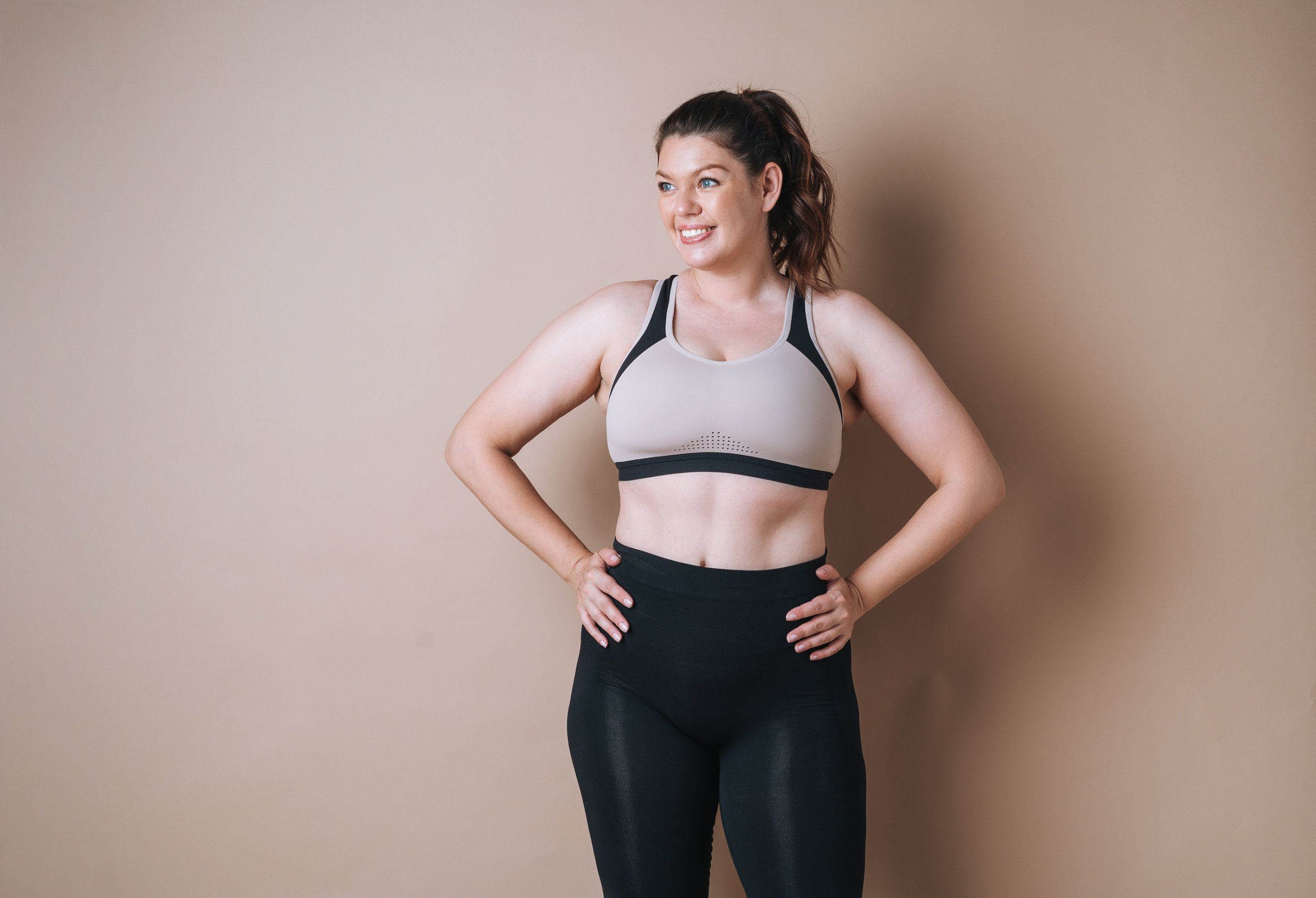 Self loving young woman plus size in sport wear on beige background, body love