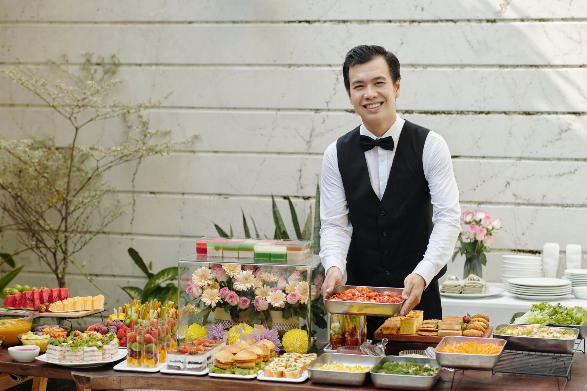 Portrait of Asian young waiter placing dish on beautifully arranged table during banquet