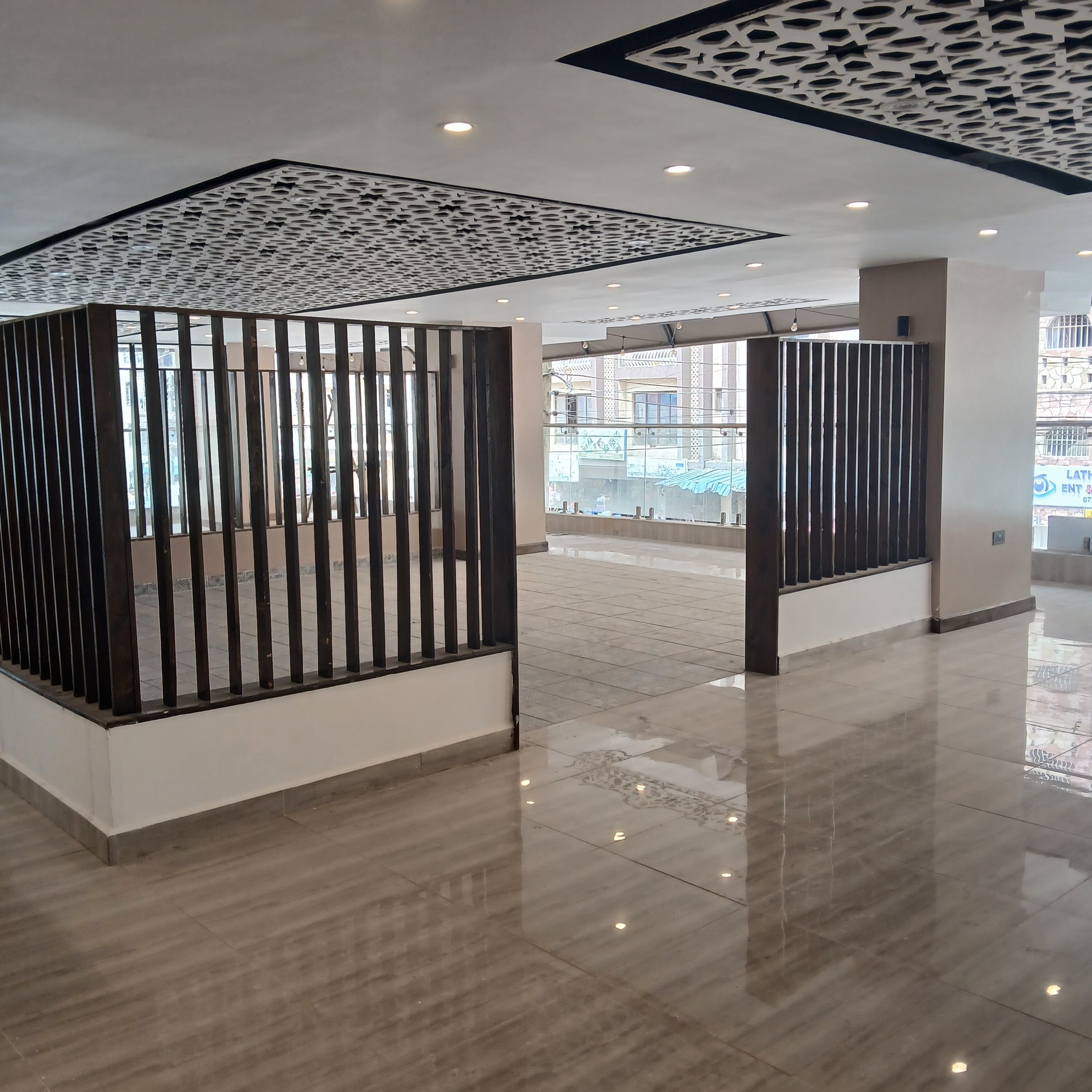 Empty modern interior with tiled floors, ceiling lights, and decorative wooden dividers in a spacious, well-lit room.