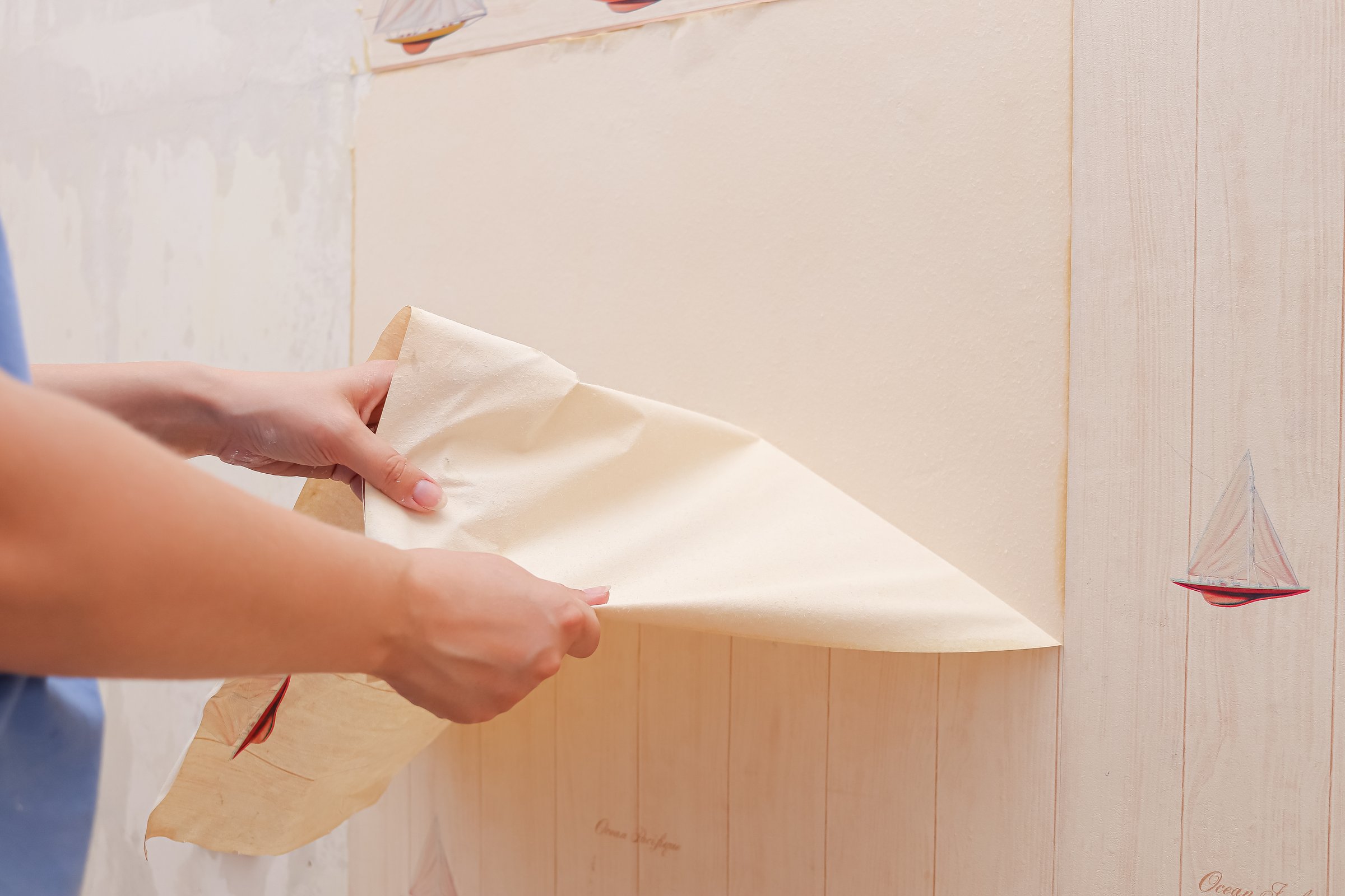 woman tears off old wallpaper in children's room. preparation for renovation, wallpaper removal. copy space