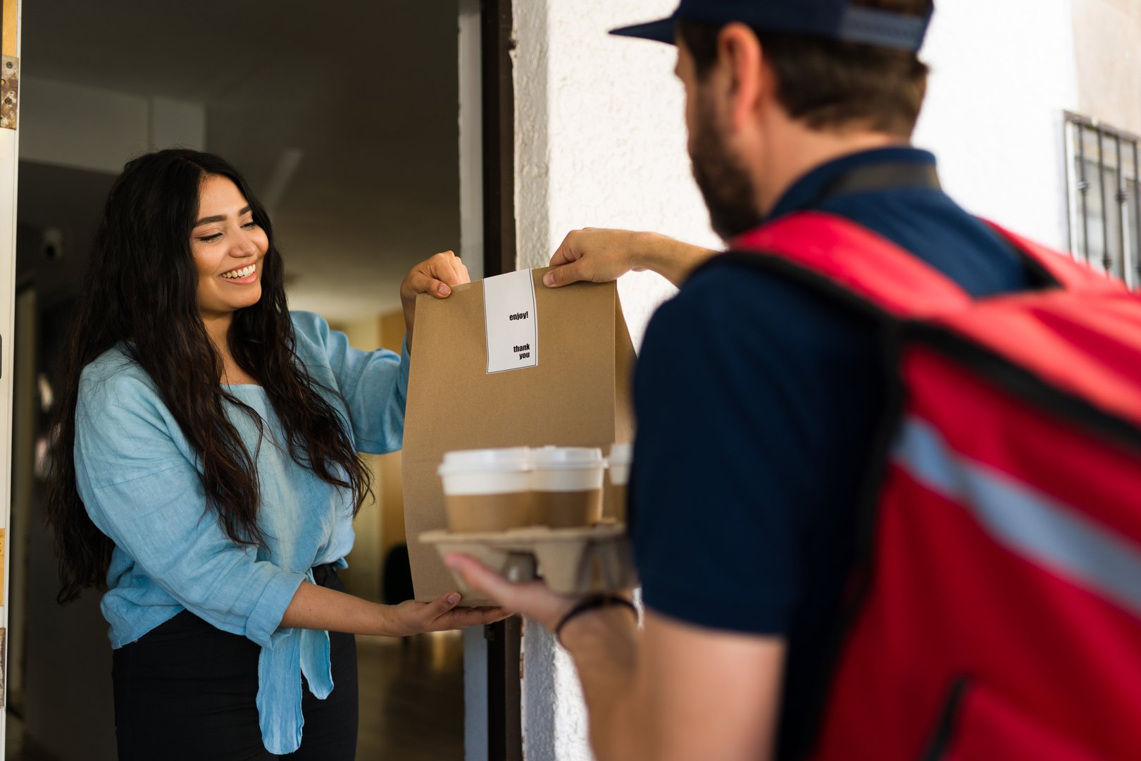 Customer smiling and taking a takeout bag and coffee cups from a delivery man, enjoying quick and easy home service