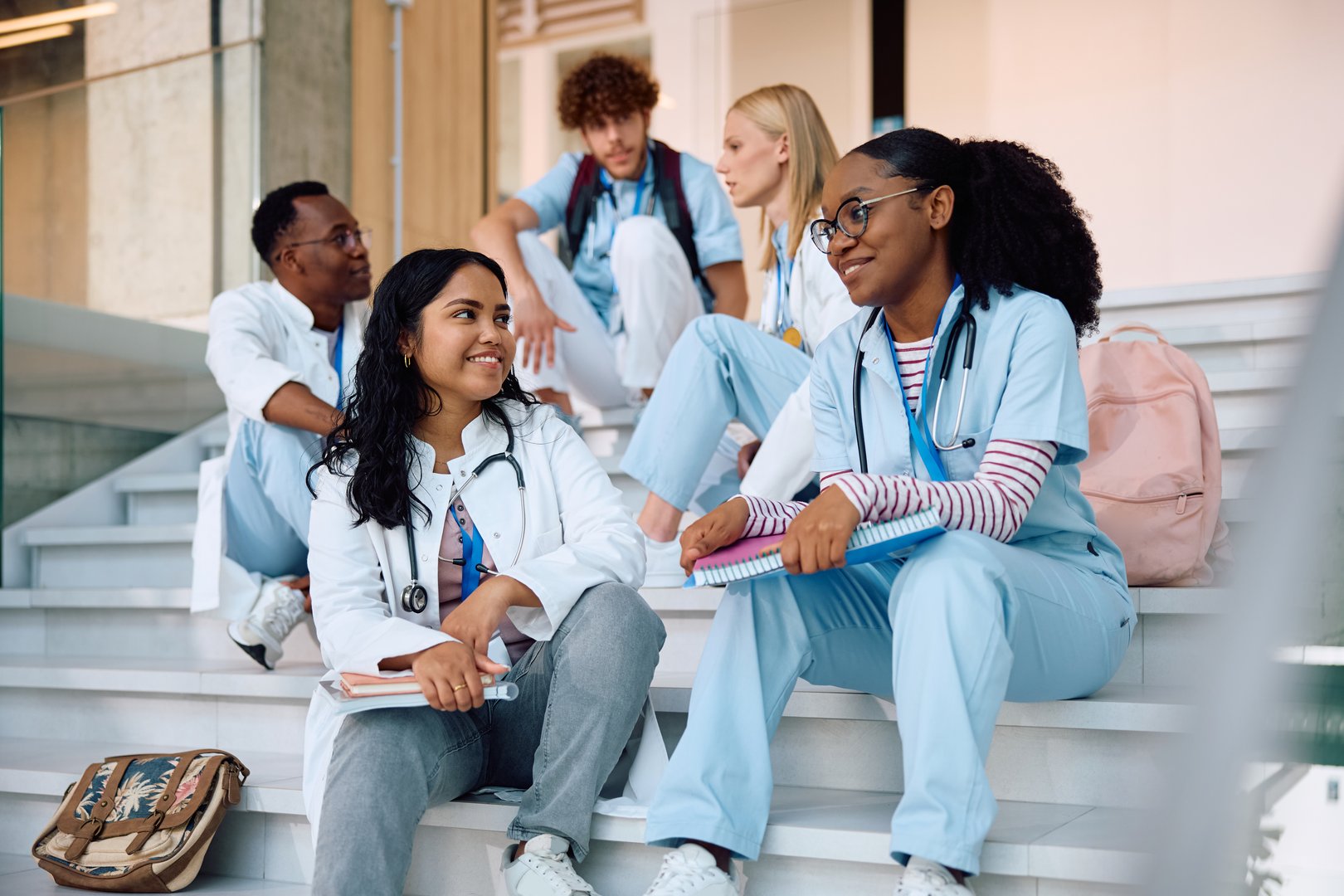 Multiracial group of students communicating while sitting on staircase at medical university.