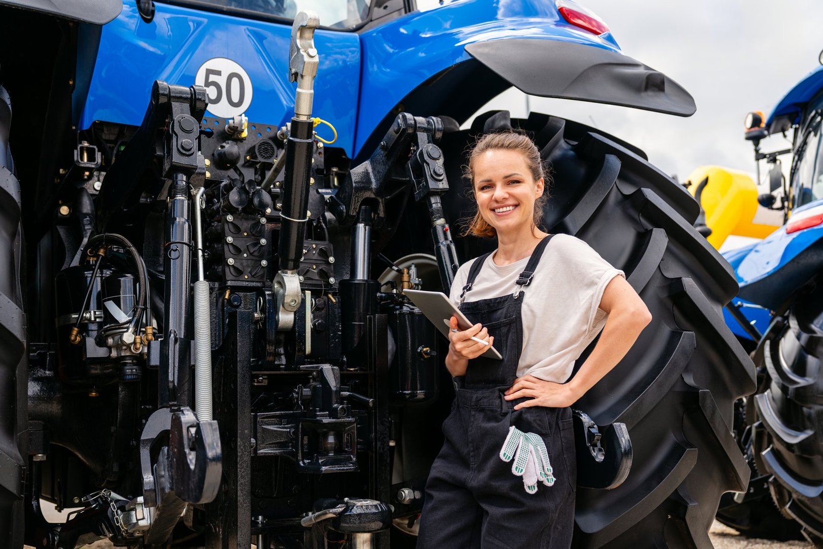 Female agricultural machinery technician using digital tablet to inspect tractor
