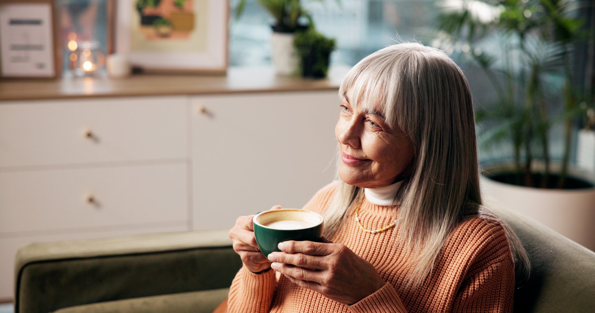 Senior woman, coffee and thinking on sofa with happy memory, daydreaming and weekend break. Smile, relax and old person with warm beverage in home for wellness, nostalgia or reflection in living room