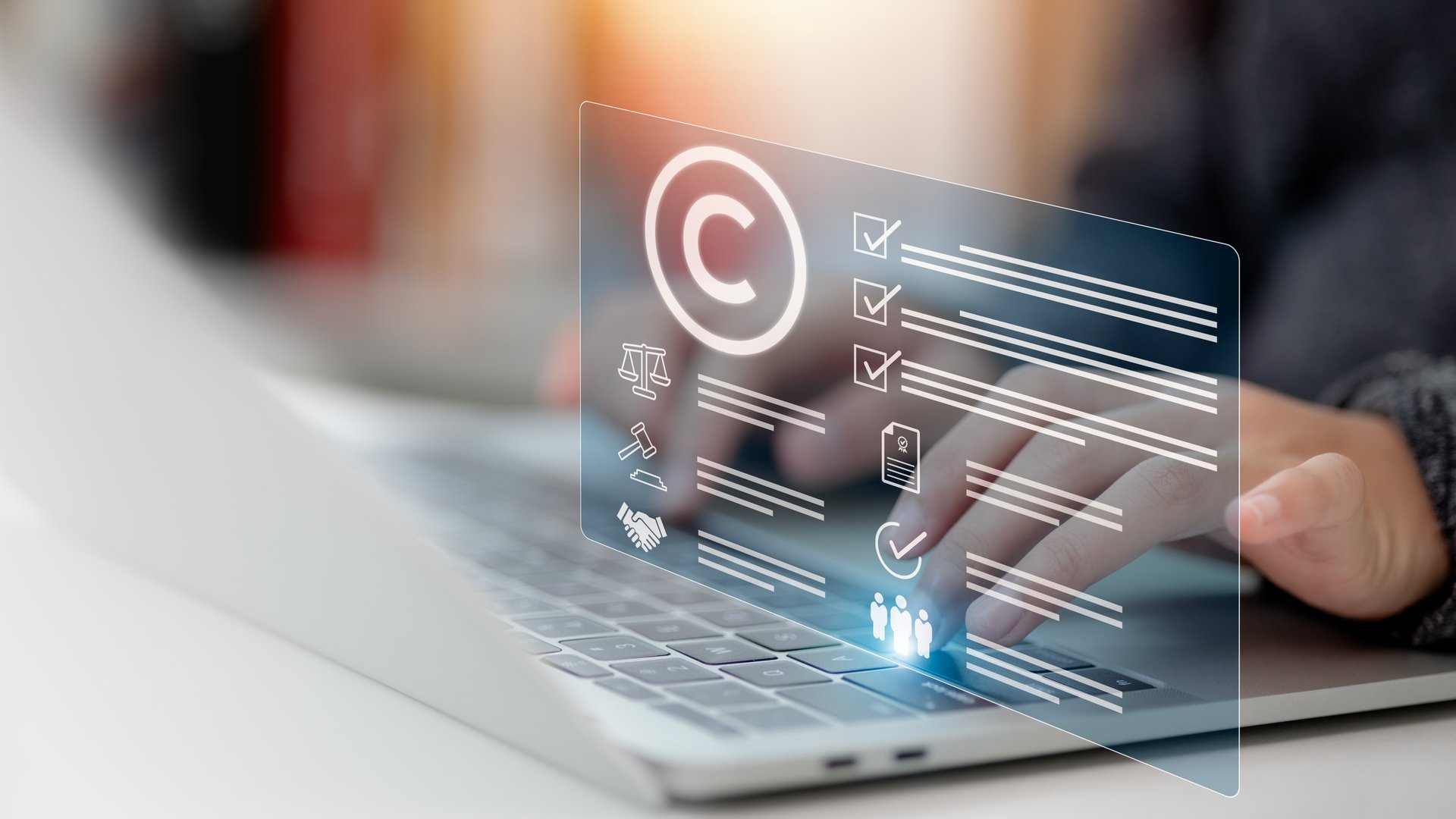Person's hand using a laptop computer on a futuristic virtual interface screen with a copyright icon background, representing the concept of copyright or patent and creation ownership against piracy crime.