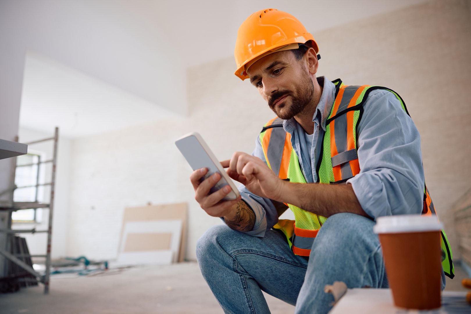 Smiling manual worker texting on cell phone while relaxing during house renovating process. Copy space.