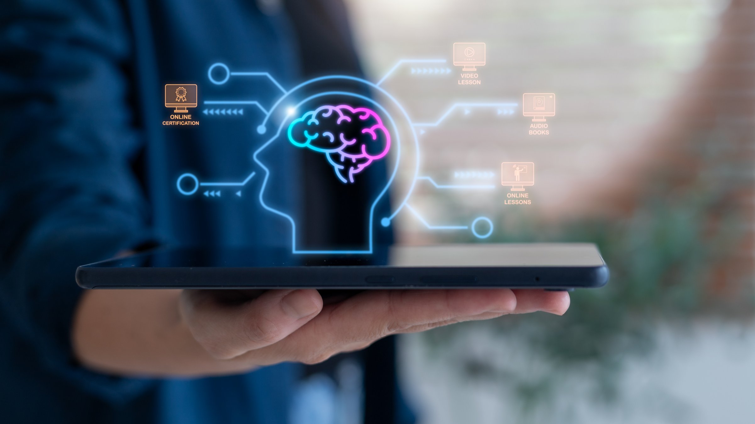 Hand holding tablet with hologram brain and e-learning icons, concept of online education, digital learning, certification courses, video lessons, audiobooks, and modern training technology.