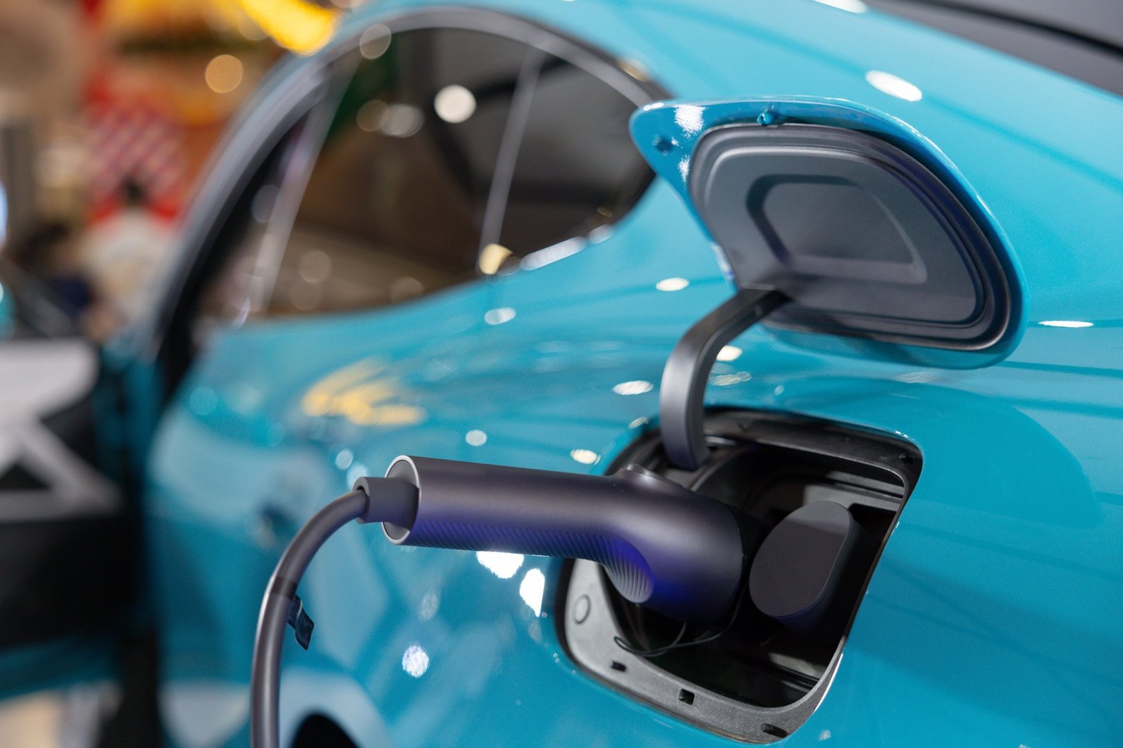 A car is being charged at a charging station. The car is blue and has a black charging port