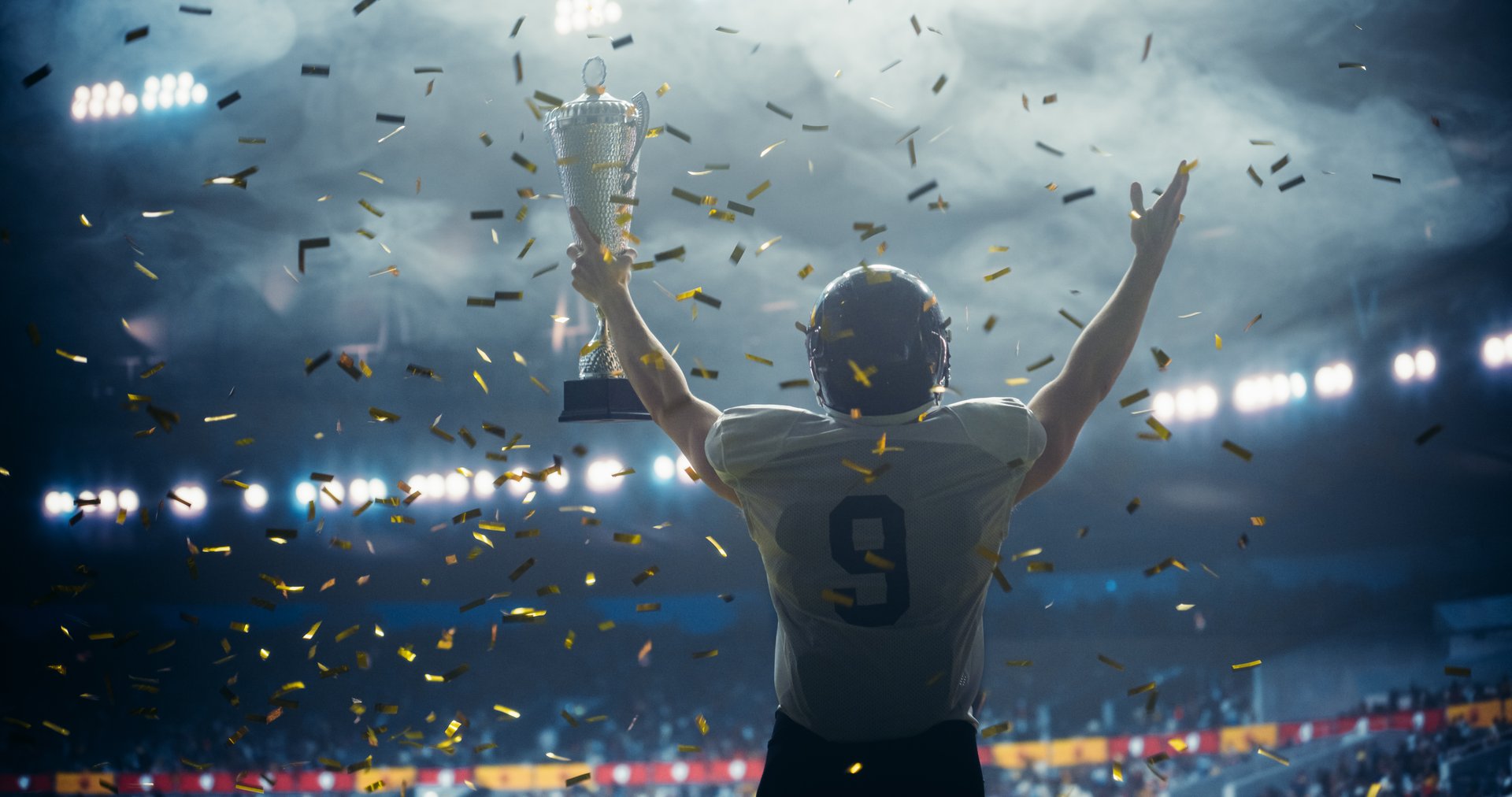 American Football Player Celebrating Victory, Holding Trophy High in Stadium with Falling Glittering Confetti and Cheers from the Sport Crowd. Footballer Full of Joy and Triumph After Championship Win