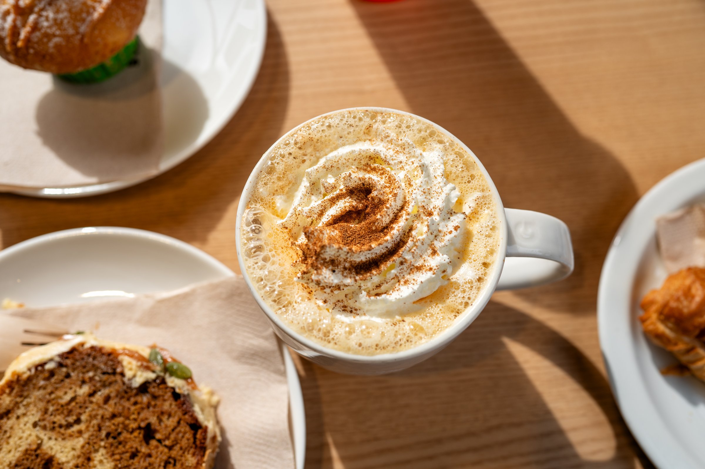 Hot pumpkin spice latte cup topped with whipped cream and slice of cake on a cafe table, cozy, autumn atmosphere.