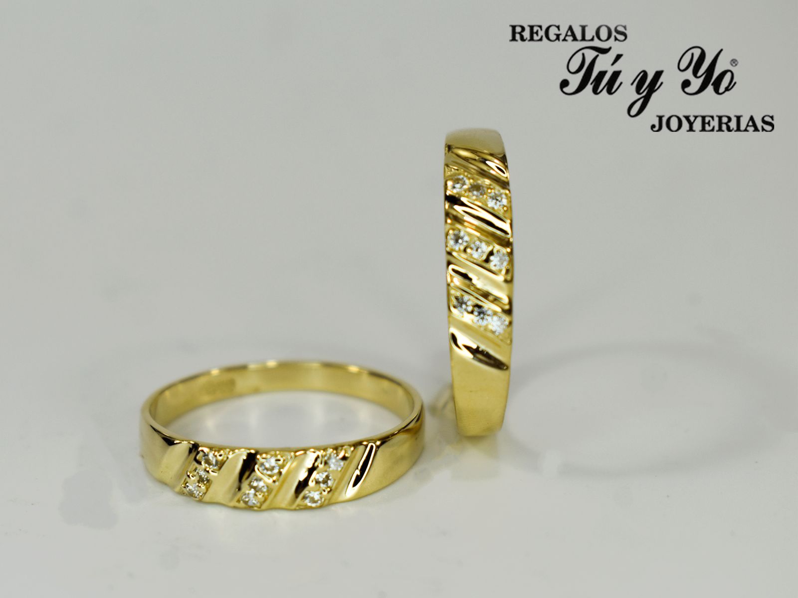 Two gold rings with diagonal diamond accents, displayed upright and flat, against a white background with a store logo.