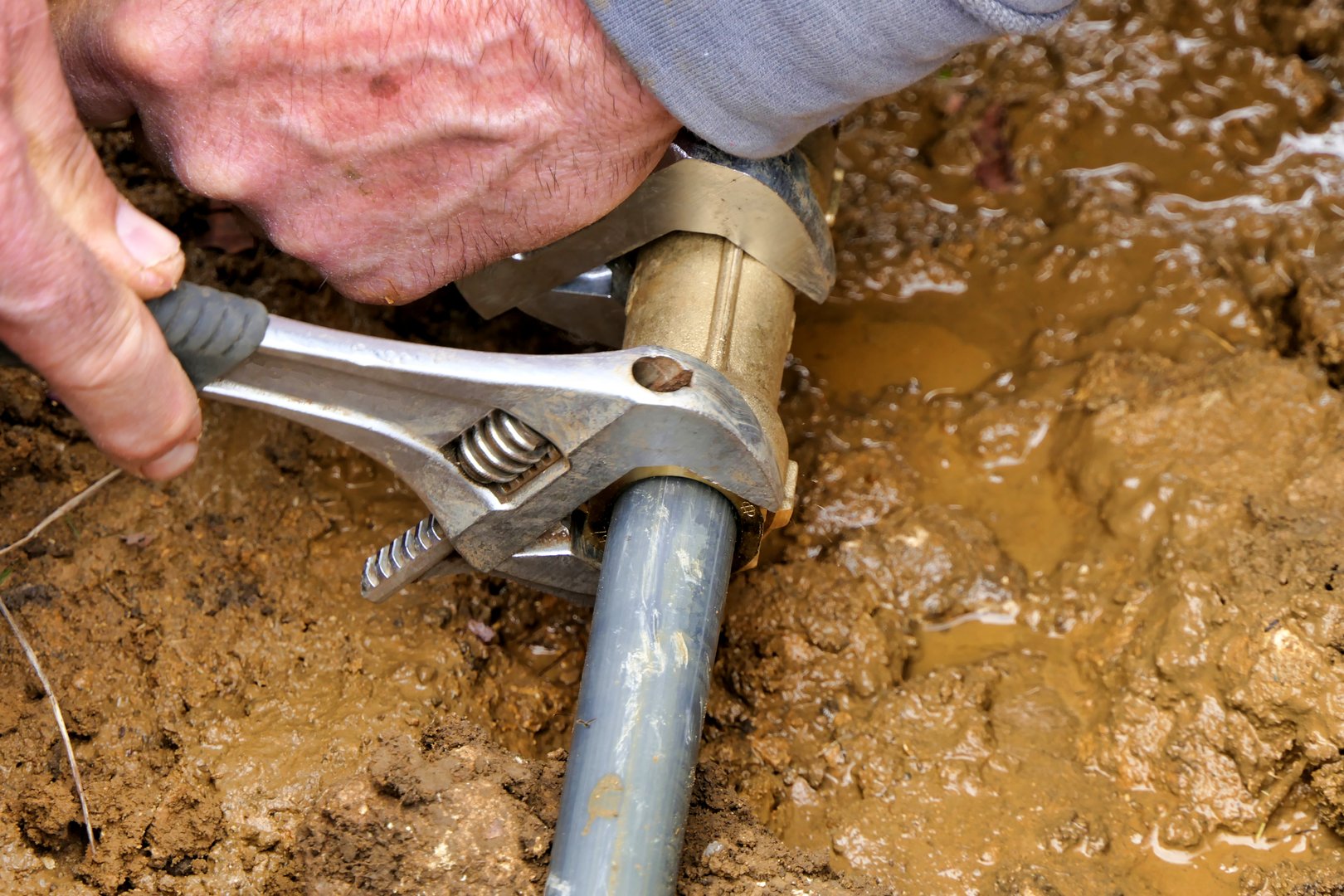 Worker attaching brass joint connector to old and new water pipes using adjustable spanners