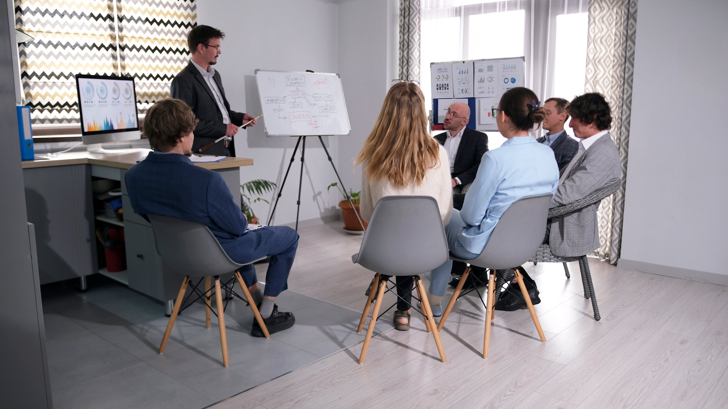 The mentor conducts training in the company of business people. A group of people are sitting on chairs in a conference room and listening to a presentation. Increase productivity and teamwork in the office