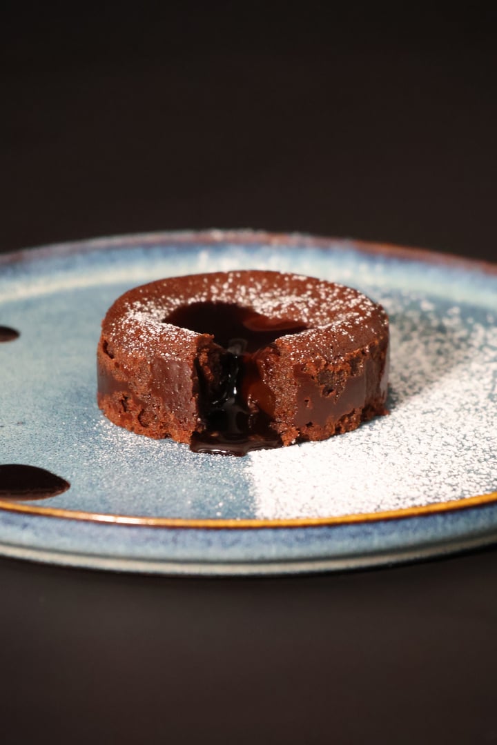 Whole chocolate fondant placed in the centre of the image, with its visible molten centre. Photograph of a gourmet dessert, ideal for illustrating pastries, sweet dishes and chocolate specialities.