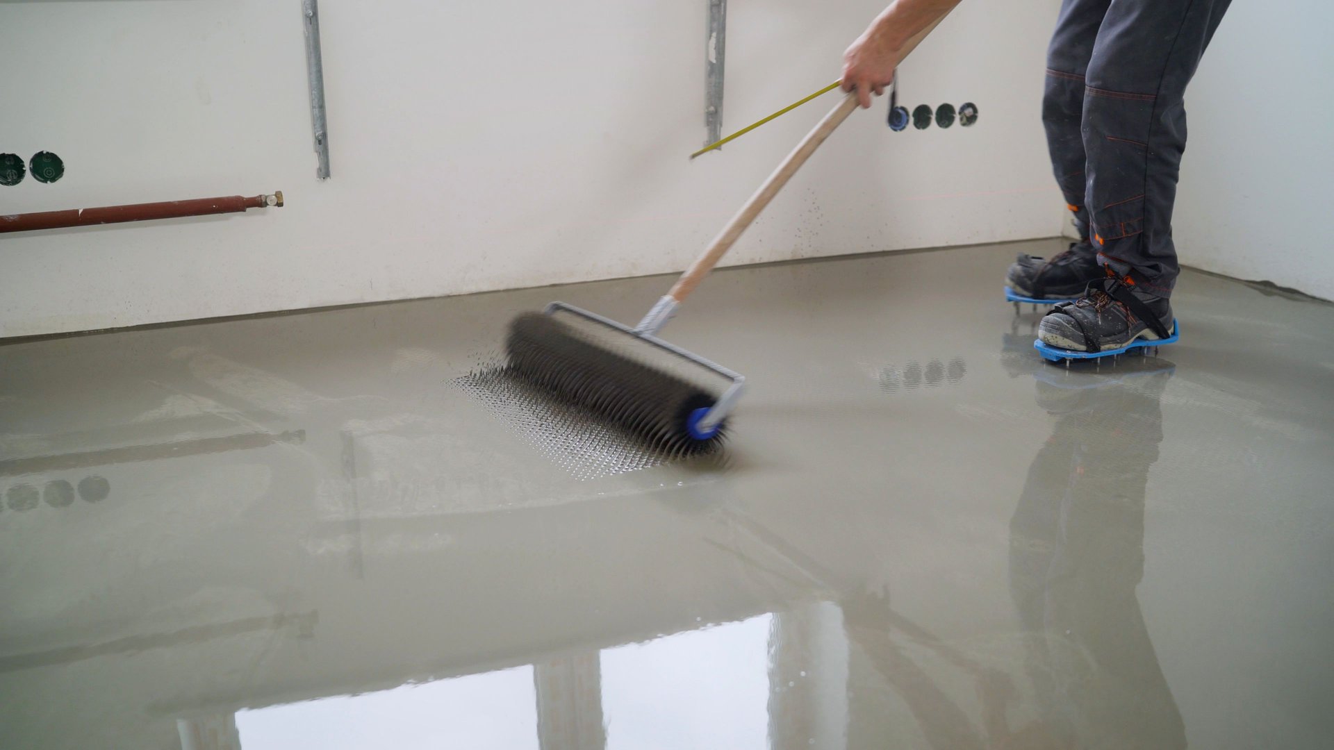 Leveling the floor with a spatula. Master with a needle roller for a new floor. concrete floor. Needle roller to remove air bubbles.