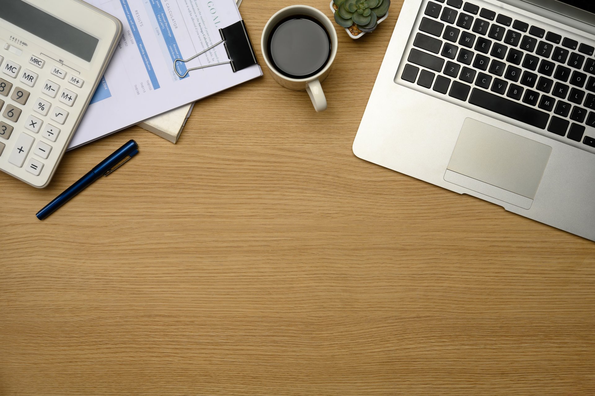 Modern office desk with laptop, calculator, coffee, and financial documents.