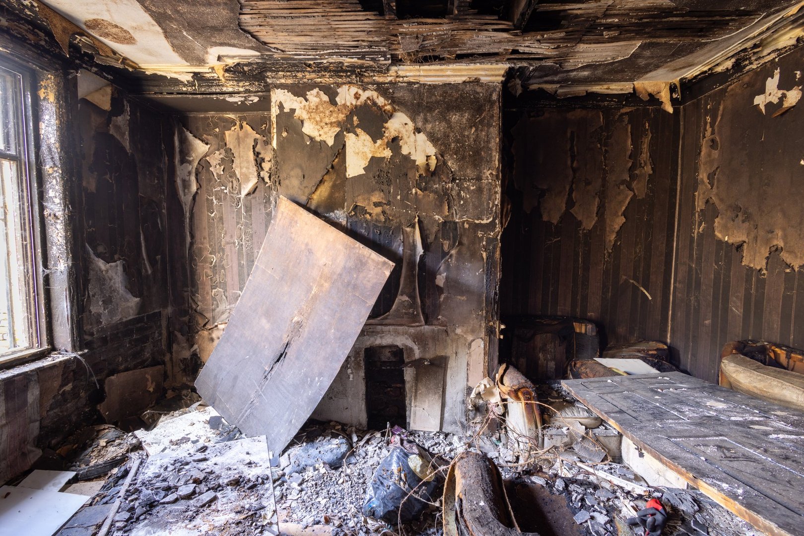 Photo of an extremely run down property that has had a massive fire showing the burnt walls fire place floors and furniture in the fire damaged living room of the British house