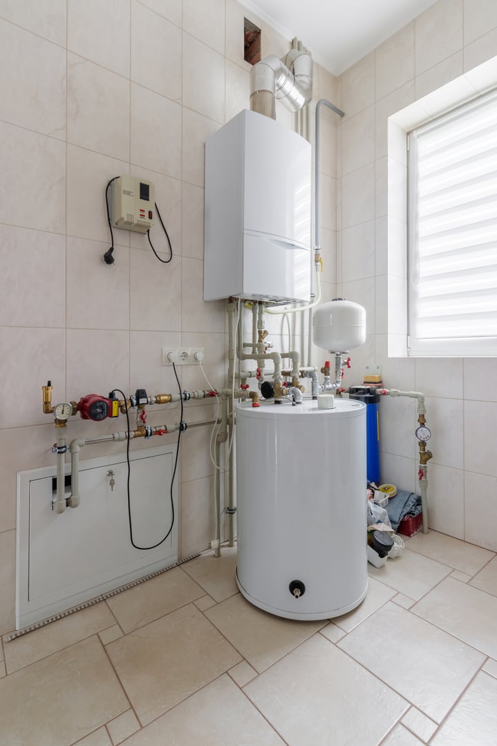 A functional boiler room with a white water heater, piping system, and a control panel mounted on the wall.