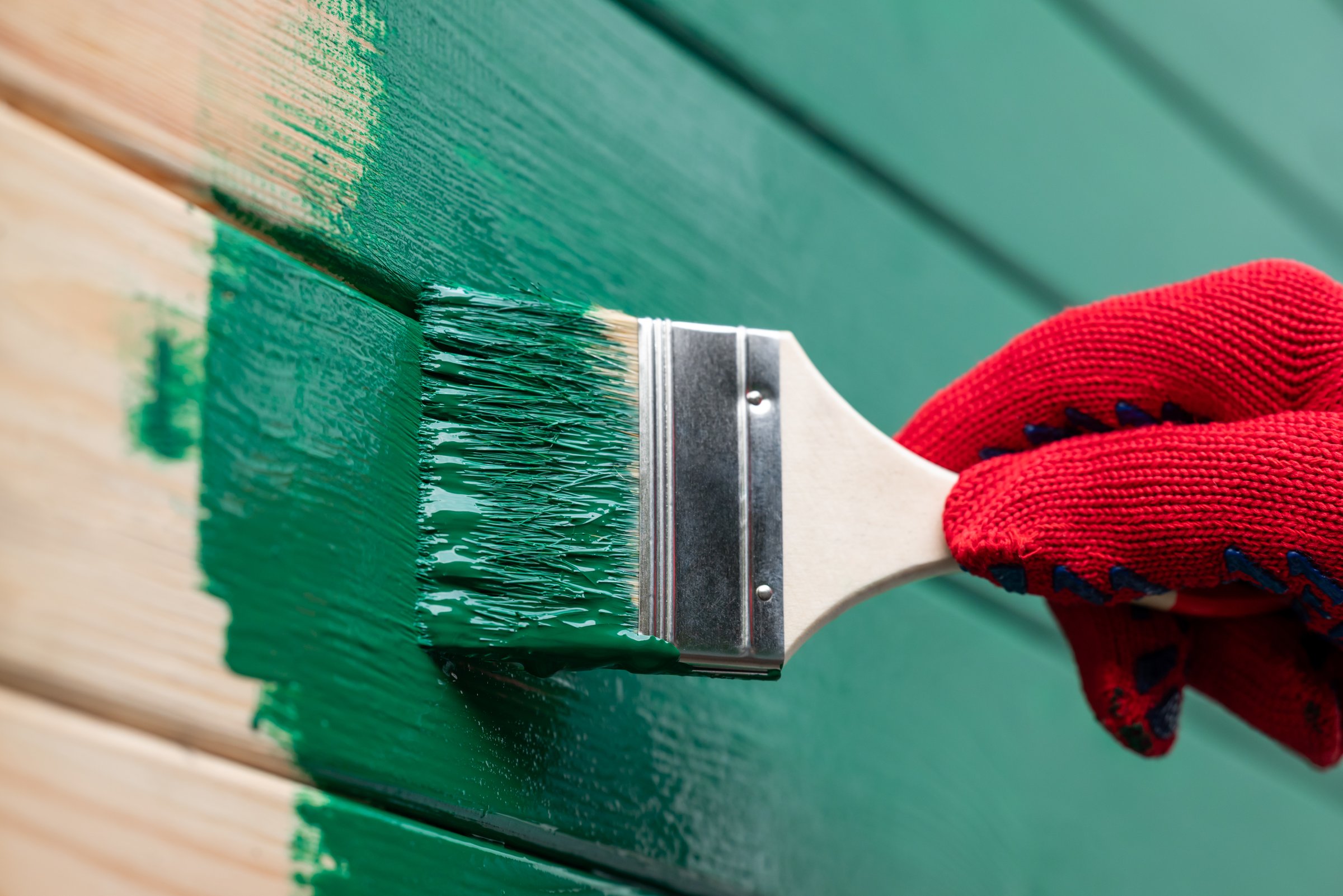Man painting wooden wall in green color, renovating house, new facade