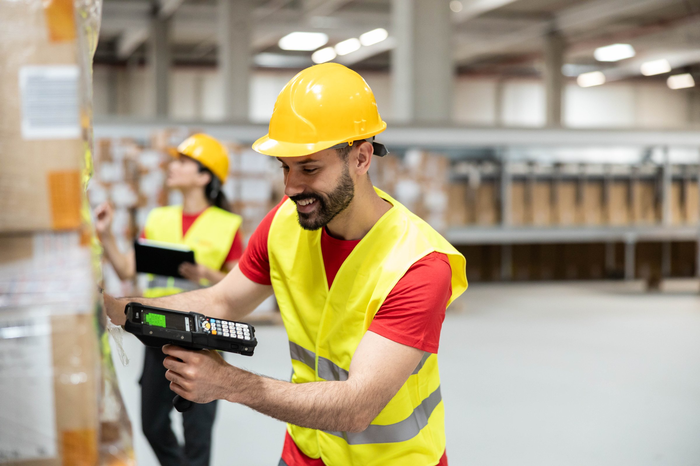 A cheerful worker scans boxes in a warehouse using a handheld device, showcasing efficiency and teamwork in logistics.
