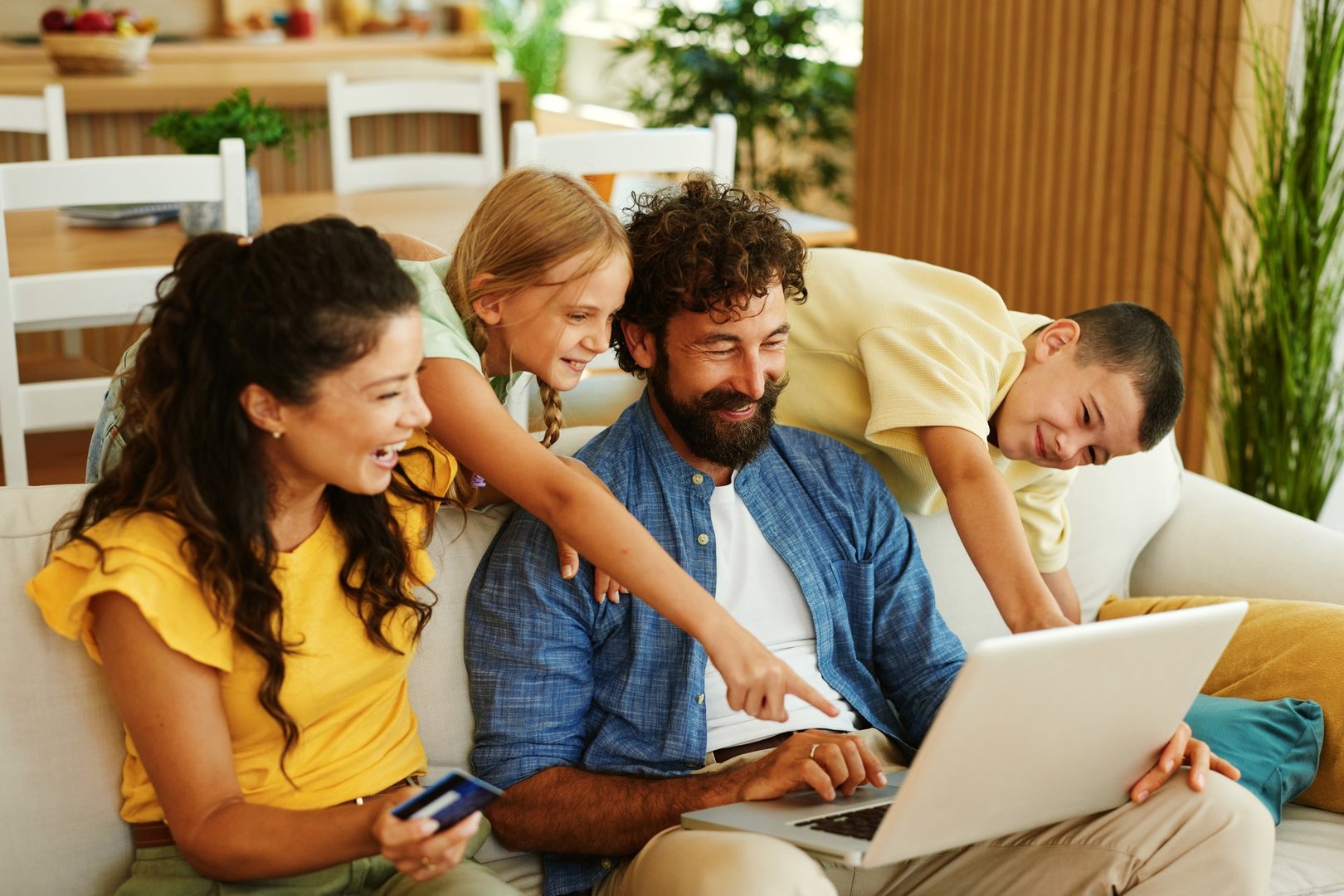Cheerful family enjoying online shopping together, using laptop and credit card on sofa at home