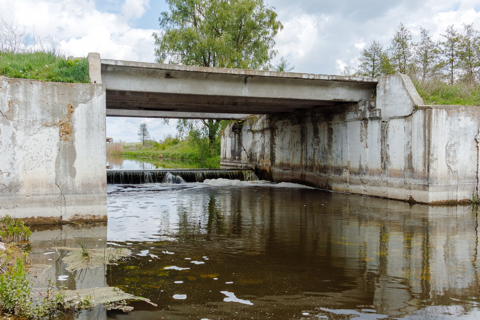 A reinforced concrete bridge spans a controlled water channel with a low-head weir, used for flood management and water flow regulation.