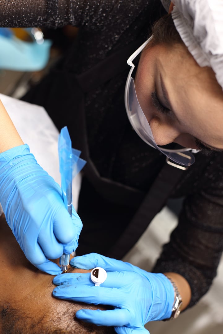 Professional Beautician woman applying Tottoo, Brow Microblading to Black african customer eyebrows to make permanent color makeup or tattooing line look real in beauty salon, copy space for text logo