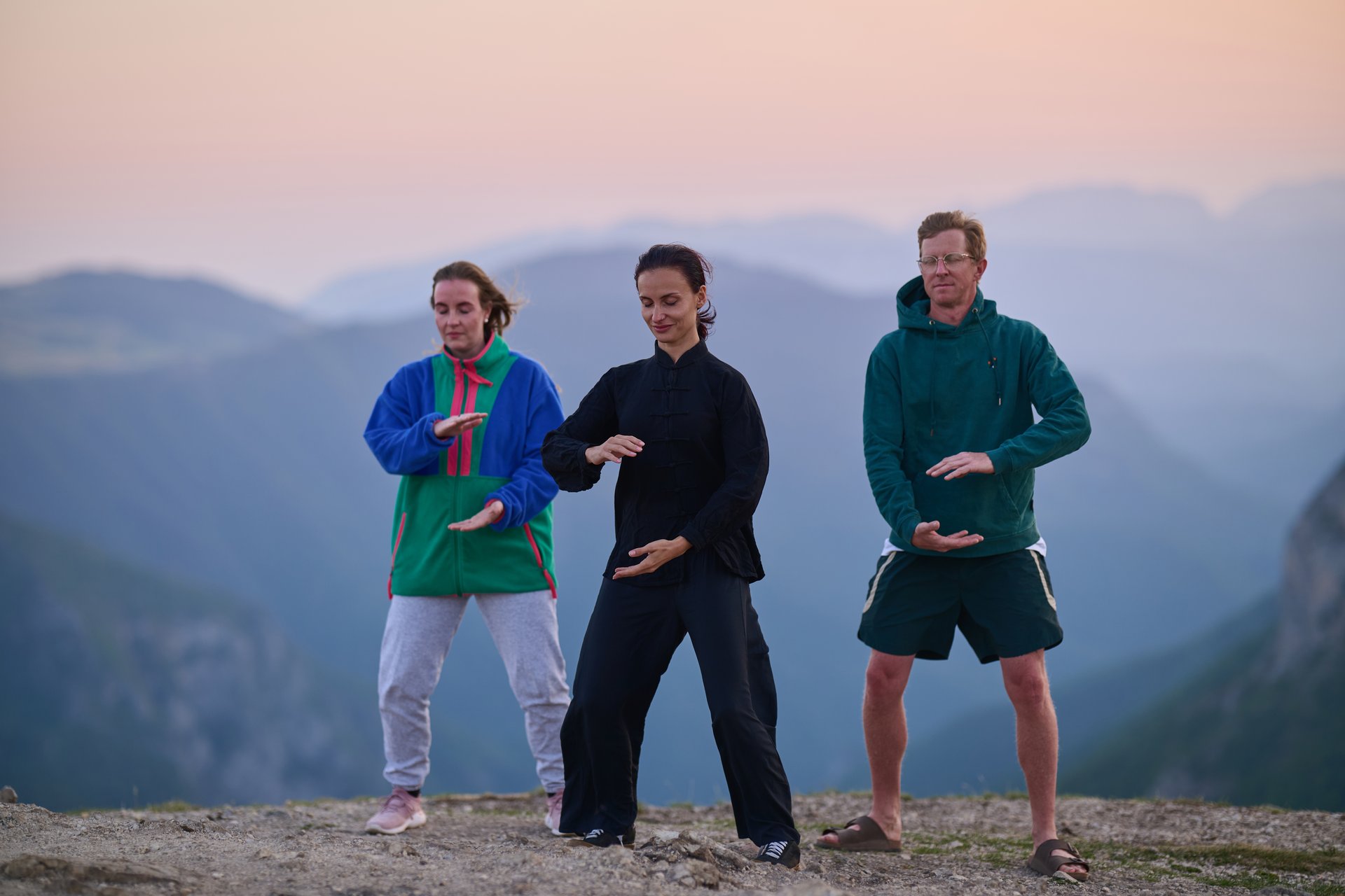 Group of people practicing Tai Chi outdoors at sunrise on mountain, performing slow meditative movements for balance, energy, health, and mindfulness in nature