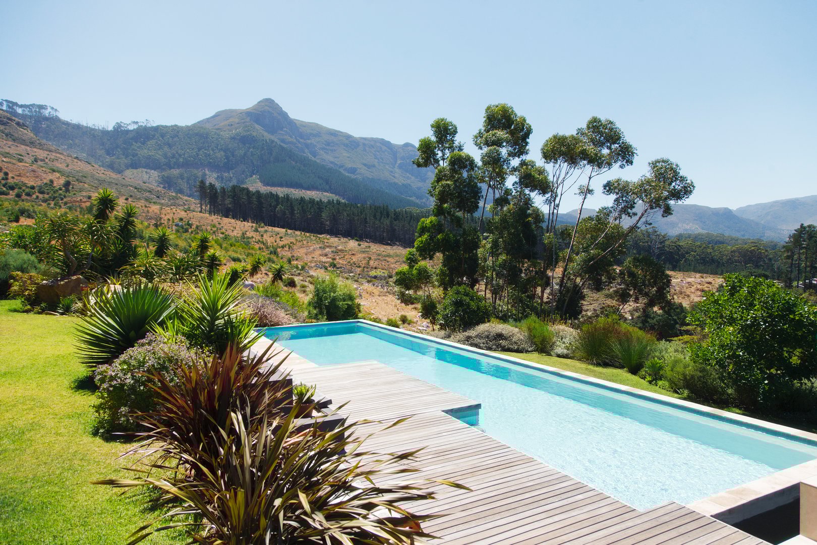 A modern swimming pool with wooden decking overlooking a scenic mountain landscape and lush greenery.