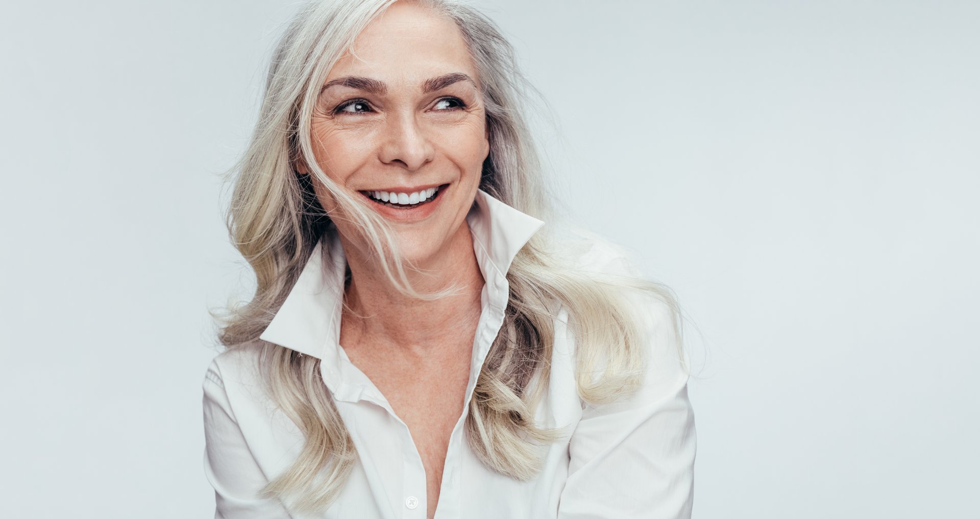 Elegant mid adult woman against white background. Stylish mature woman in white casuals looking away and smiling.