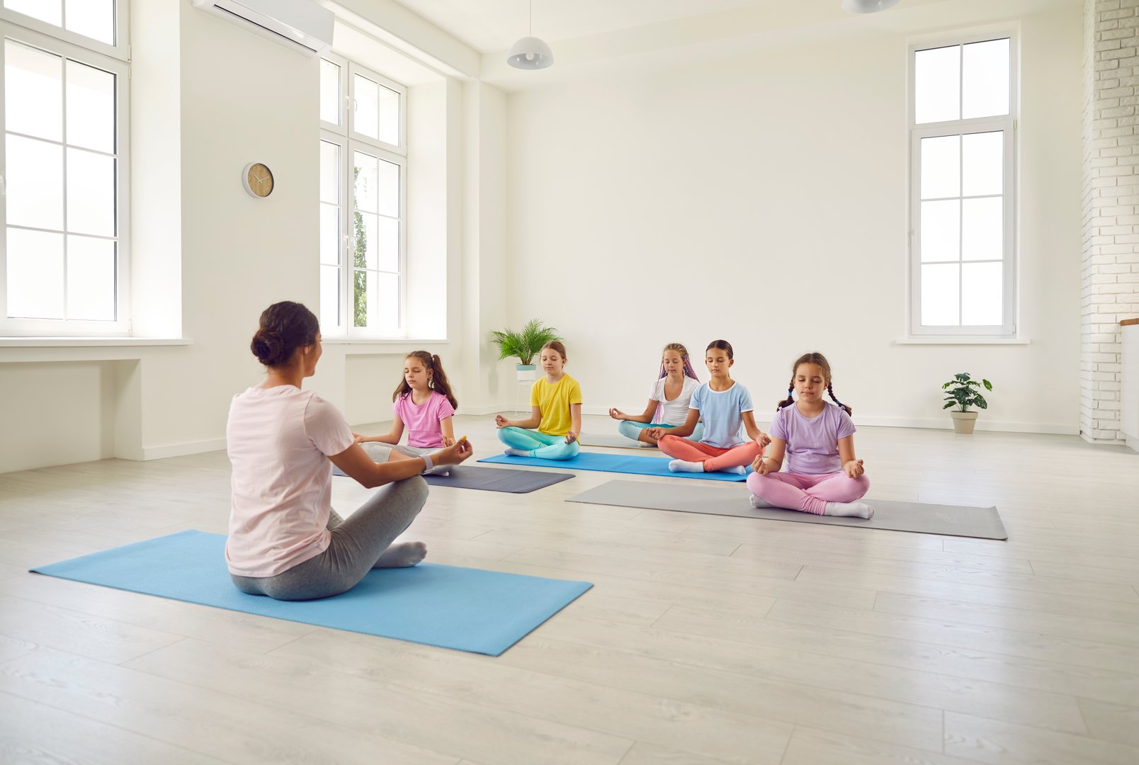 Portrait of a little kids girls sitting on the floor with their teacher and practicing yoga sitting in gym in Lotus pose with closed eyes. Children sport and active lifestyle concept.