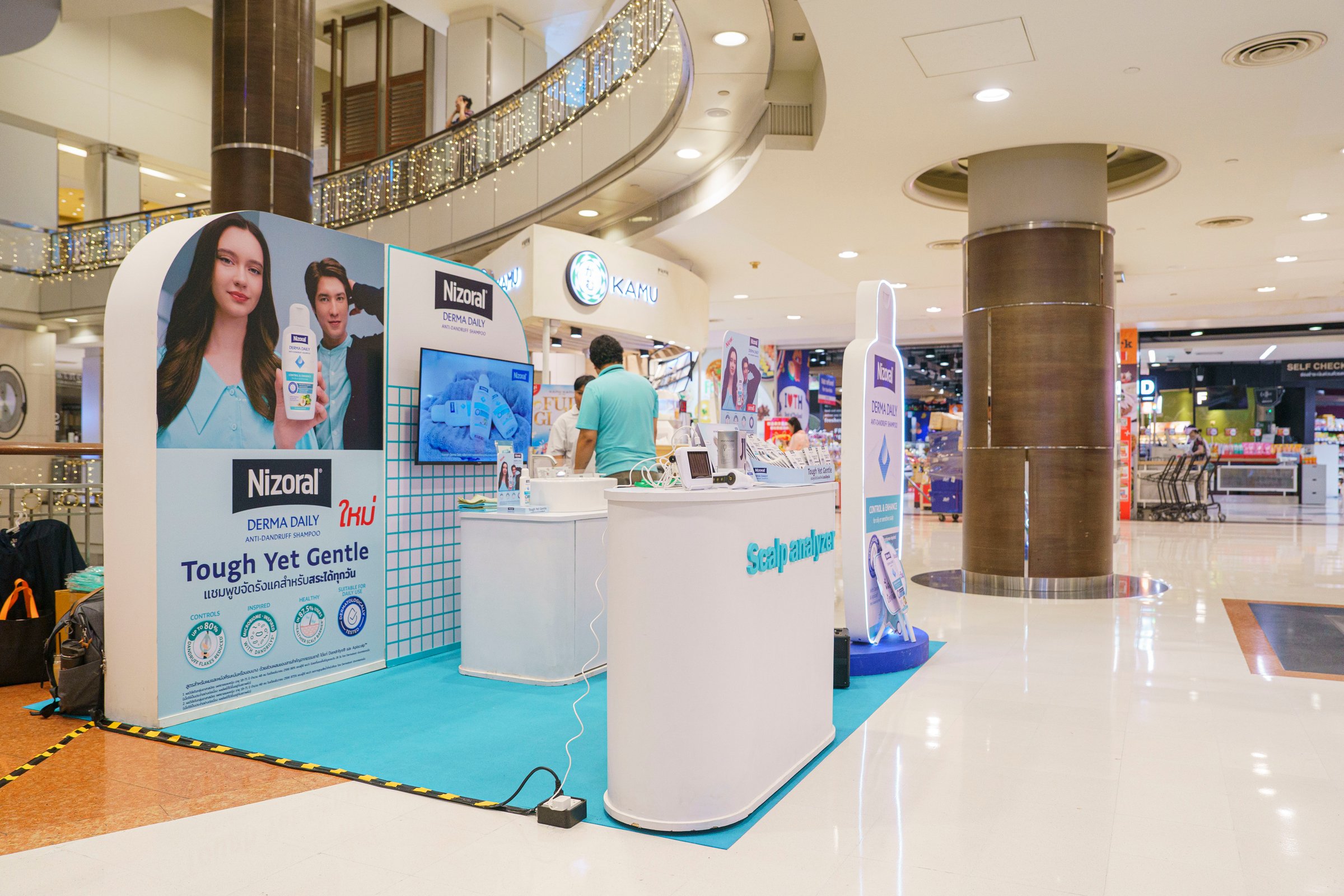 Shopping mall kiosk promoting Nizoral shampoo with posters and a counter, man working behind the display.