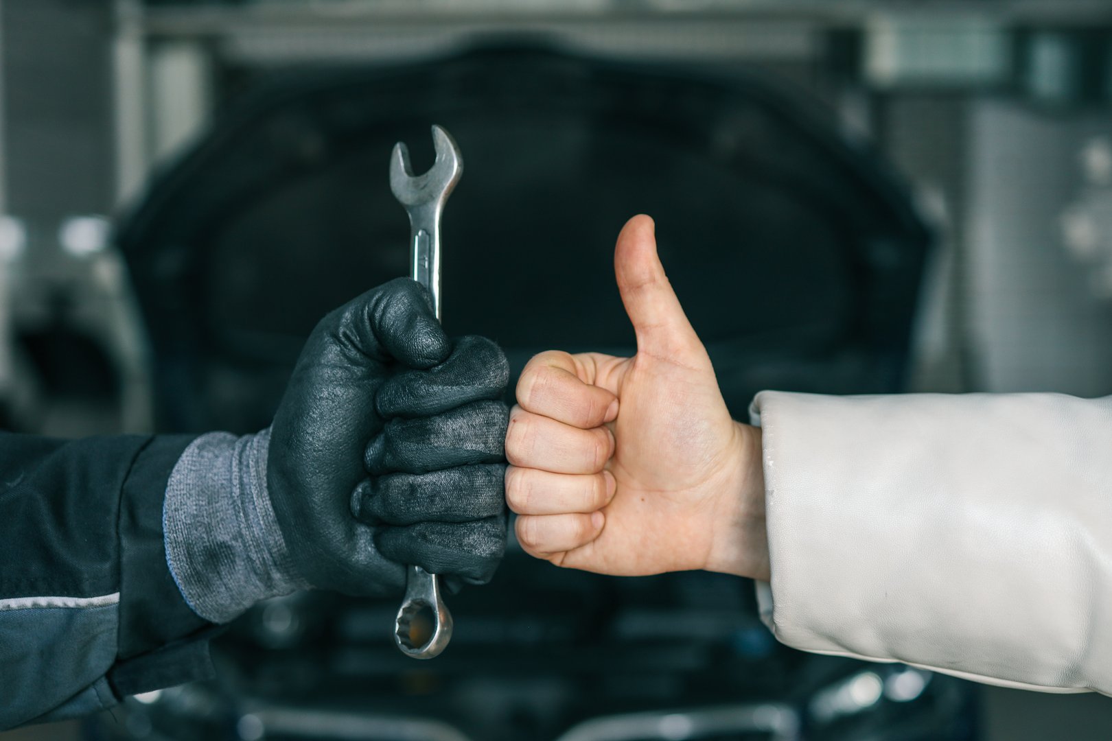 Close-up of a mechanic's gloved hand holding a wrench and a customer's hand giving a thumbs-up, symbolizing satisfaction and trust in car repair services.