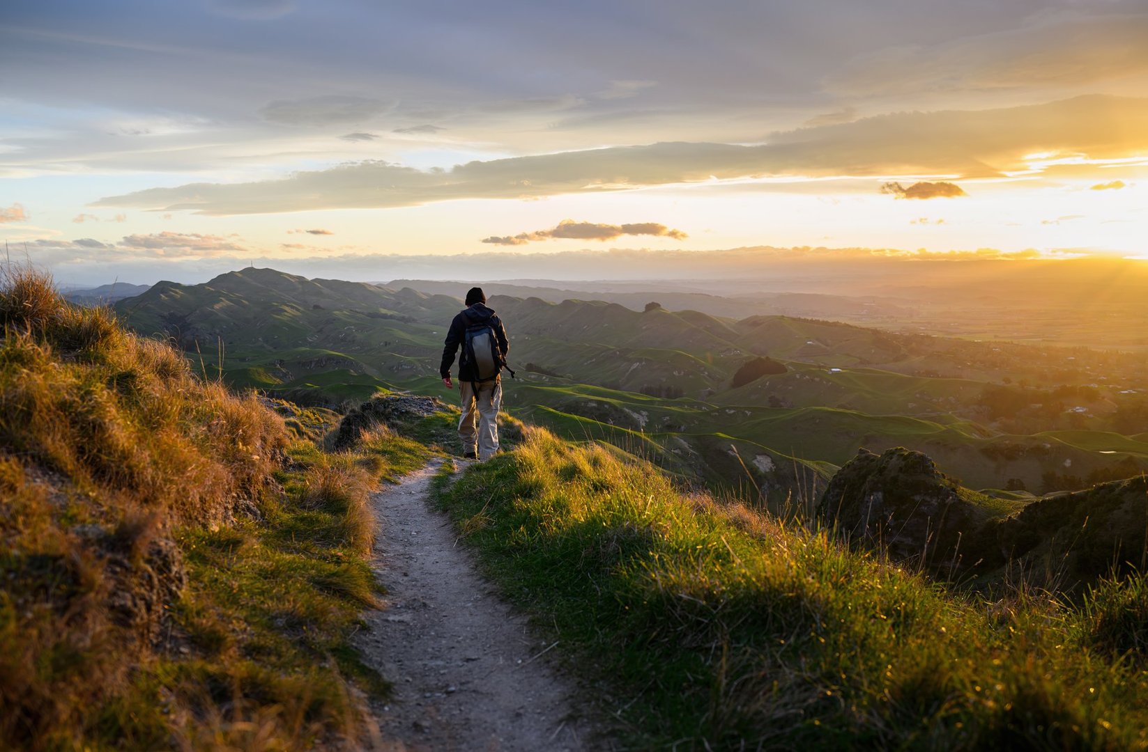 Man hiking on top of the hill with warm sunset glow on rolling hills